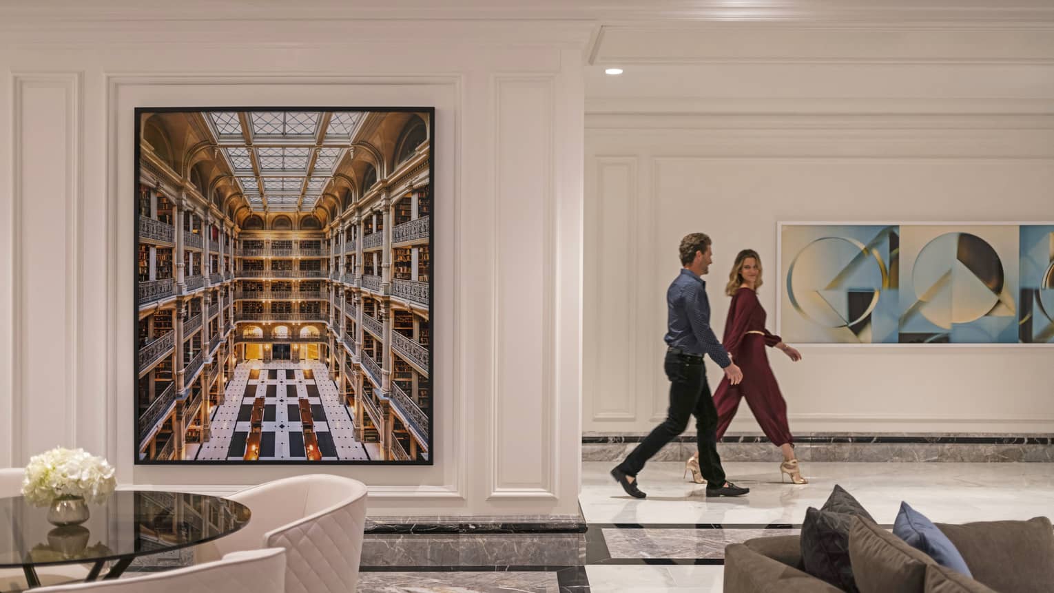 A couple walking through the hotel lobby, there is art on the wall behind them.