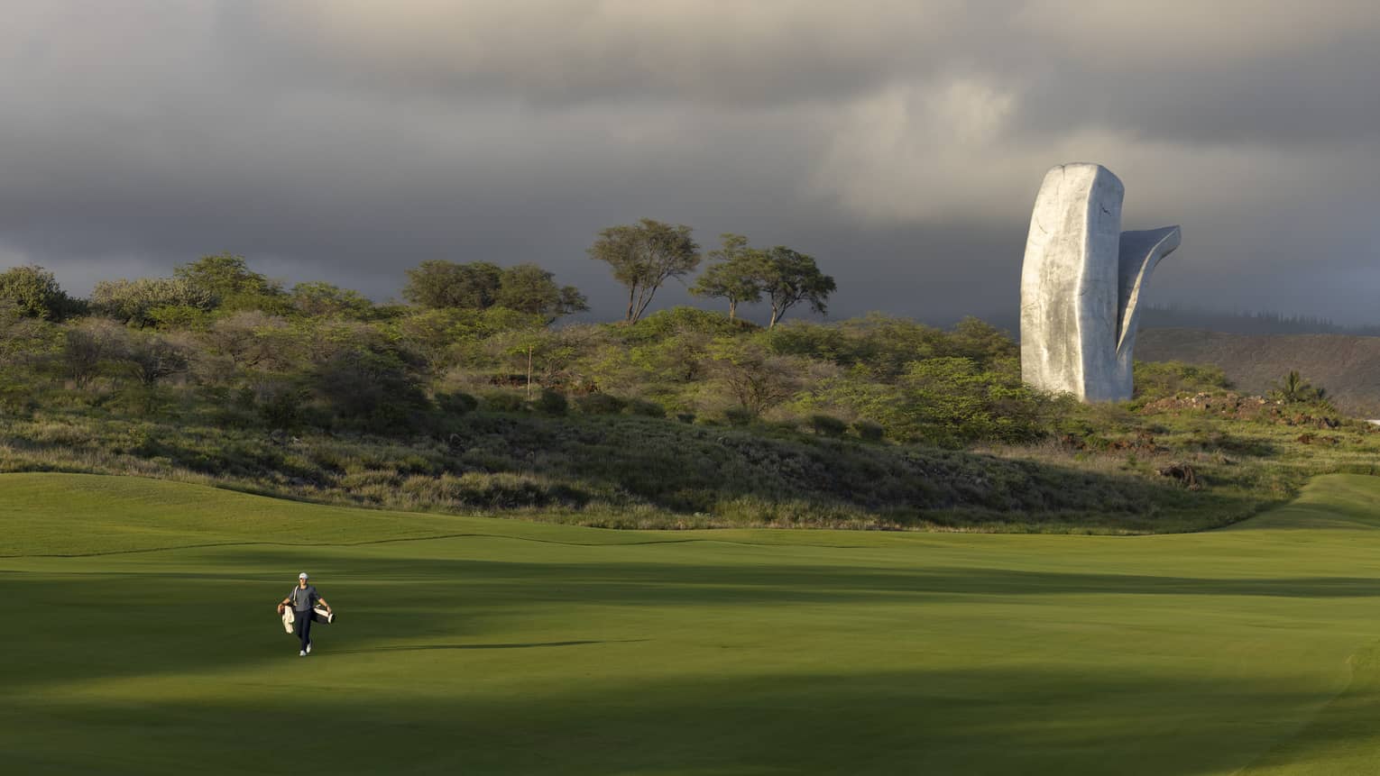 A verdant golf course with a large abstract sculpture in the background.