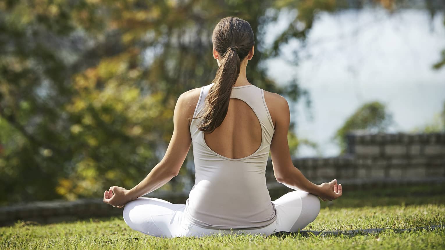 Back of woman meditating on sunny lawn