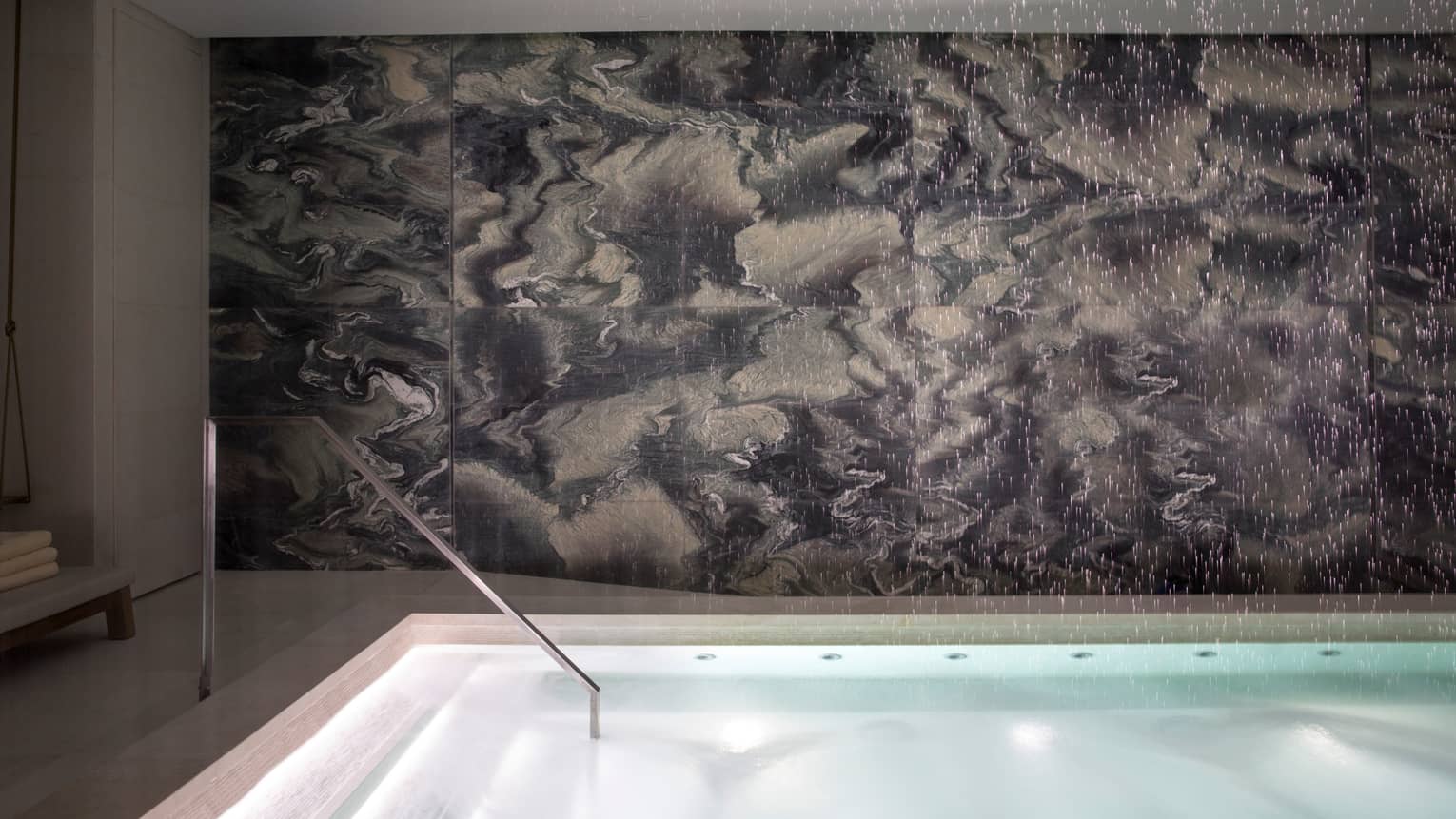 Illuminated water, steps of indoor swimming pool in front of grey marble wall