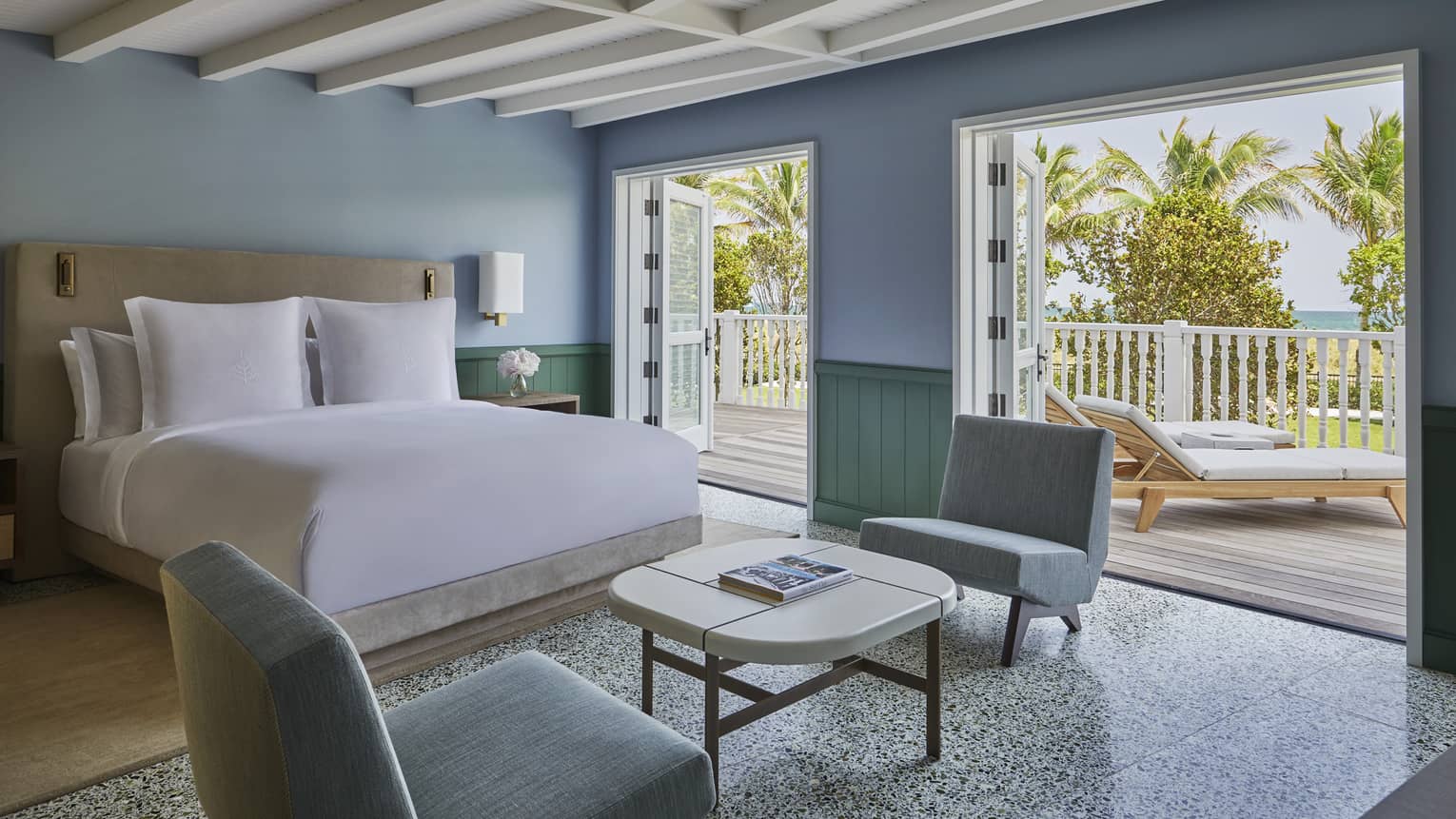 A hotel room with blue walls, white wooden beamed ceiling, and two large entrances to an private wooden patio