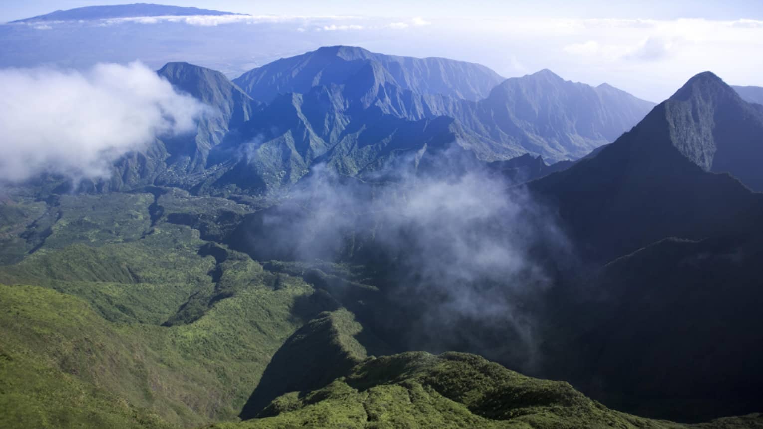 Clouds hover over green volcanic mountains