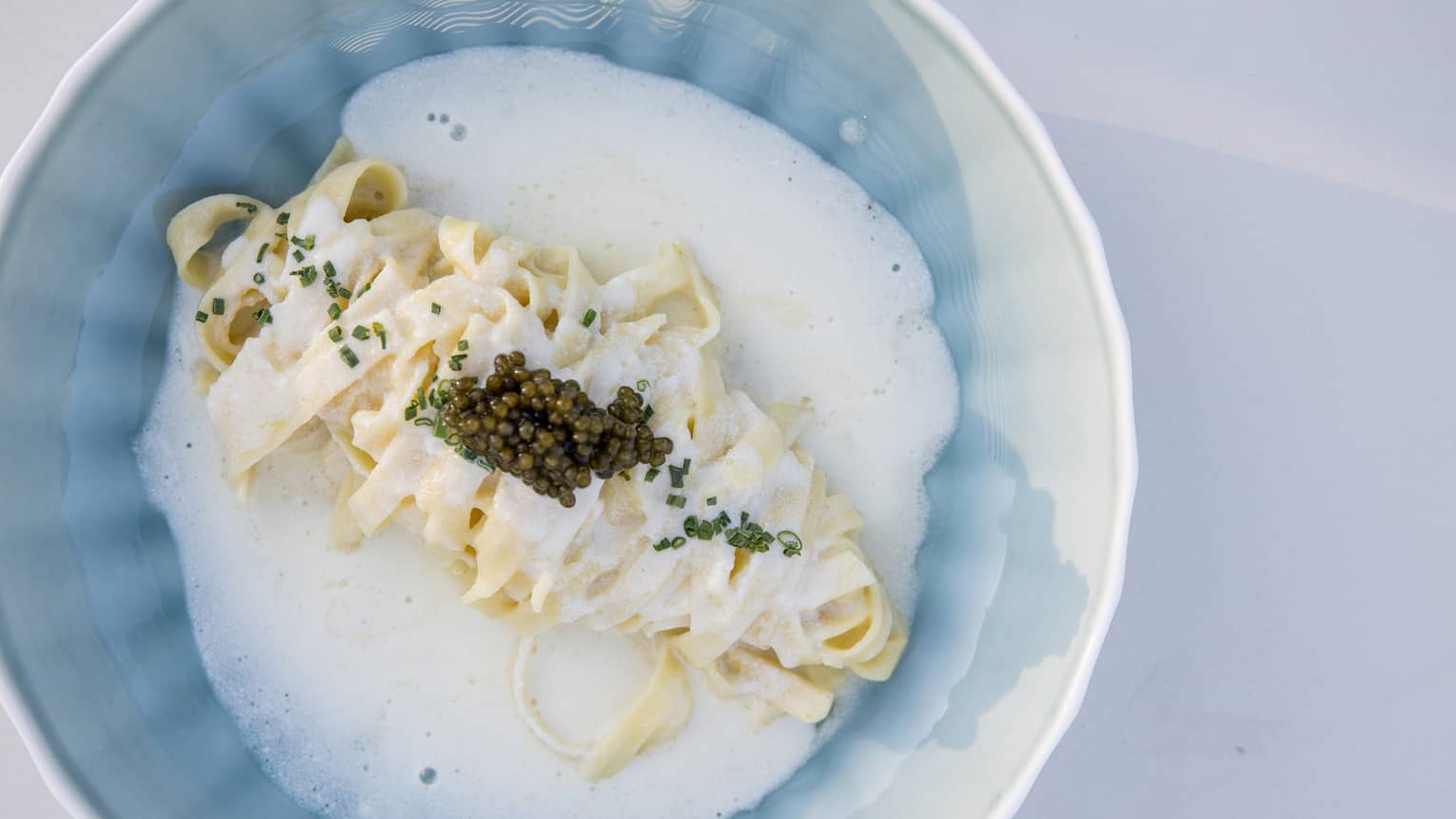 Bowl of linguini tossed in a bright citrus sauce with agrumato olive oil and topped with caviar and chives
