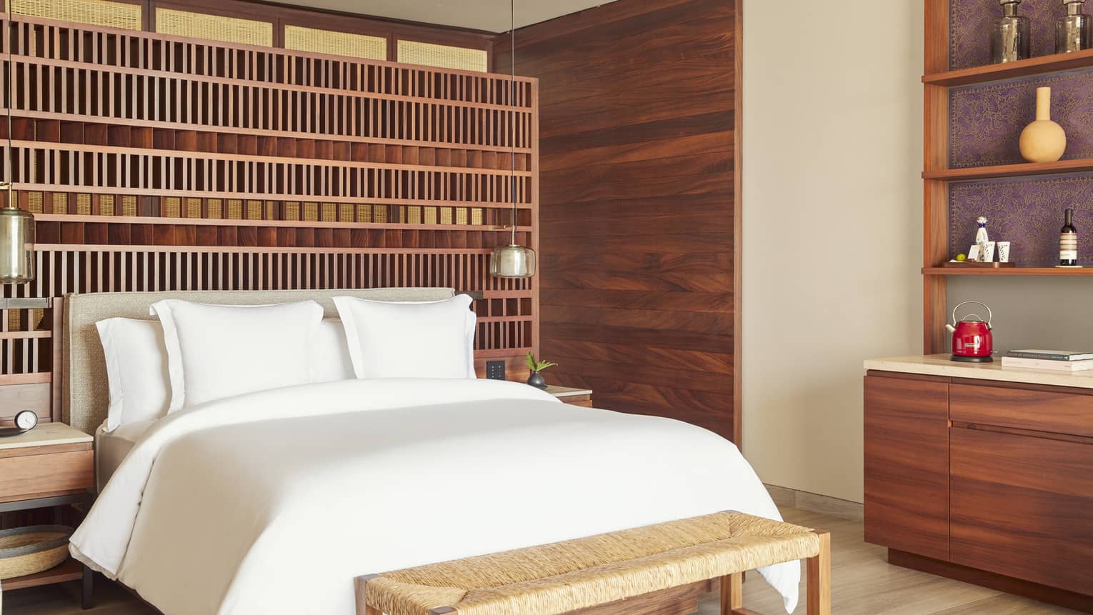 Guest room with King bed and white linens, rattan foot bench, wood-panelled walls with built in shelves