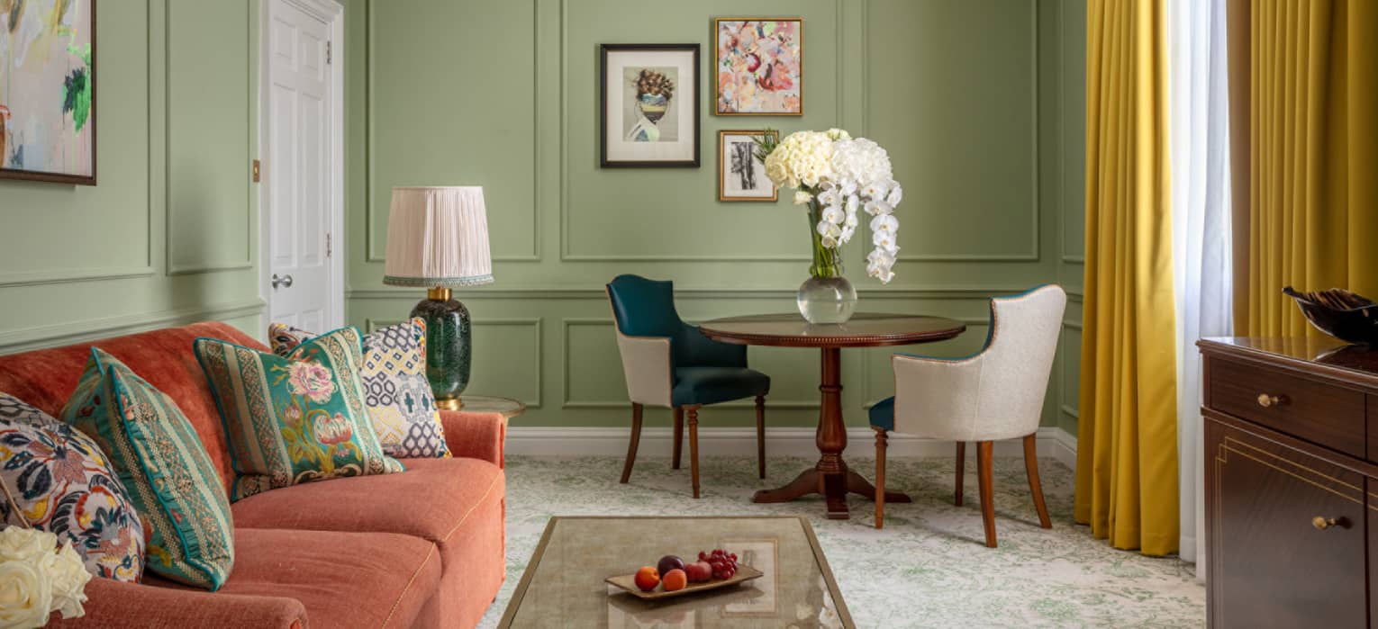 Guest room with red couch, coffee table, small round table with two leather chairs, avocado-coloured walls, window with yellow drapes