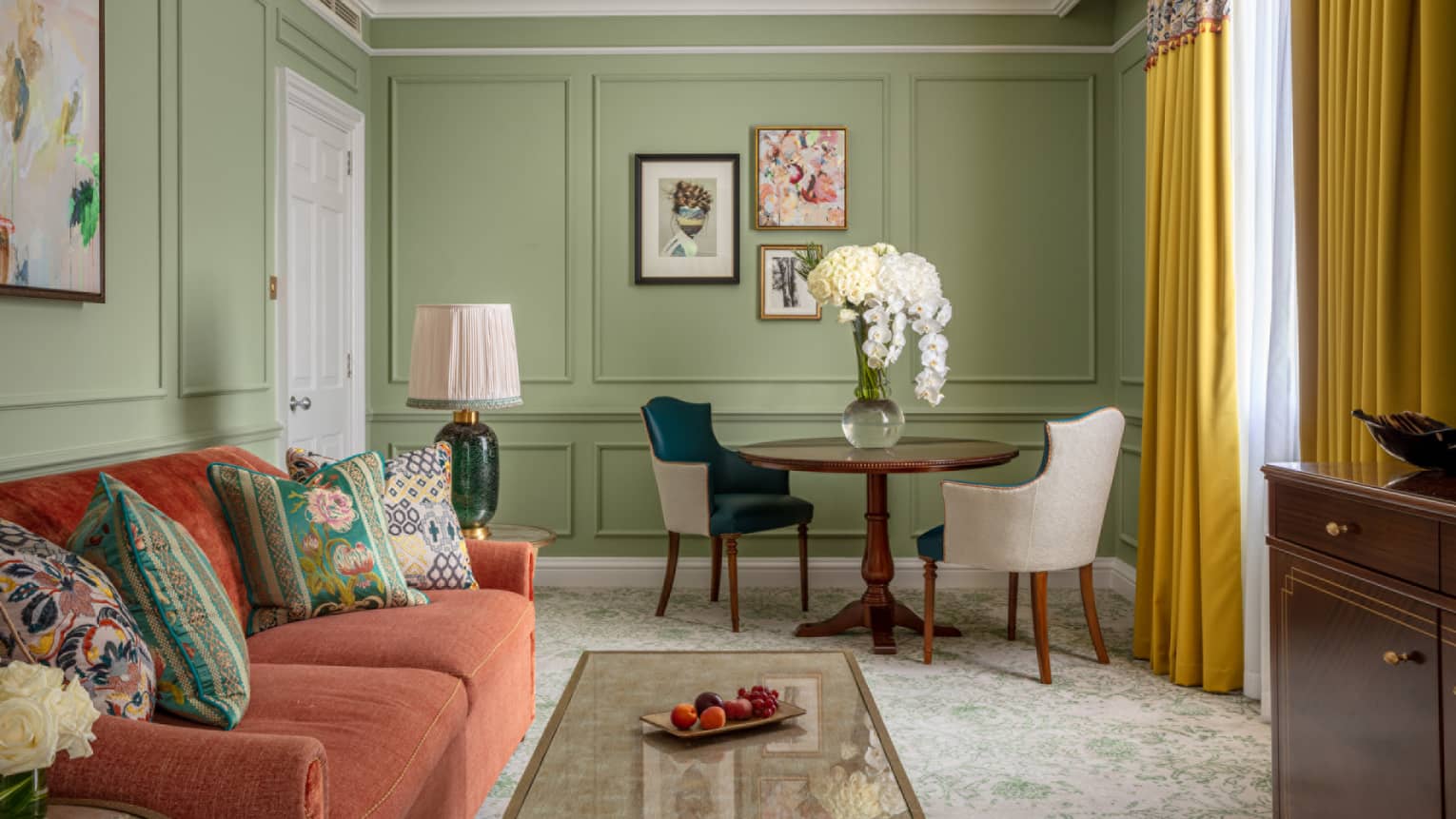 Guest room with red couch, coffee table, small round table with two leather chairs, avocado-coloured walls, window with yellow drapes