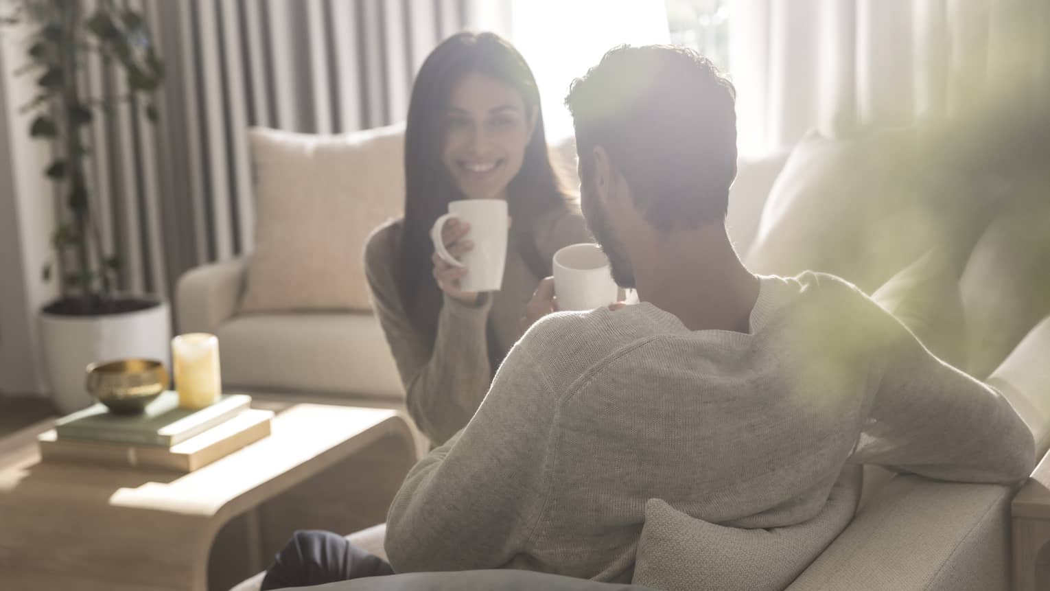 Two guests sitting on the couch in a living room and drinking out of mugs