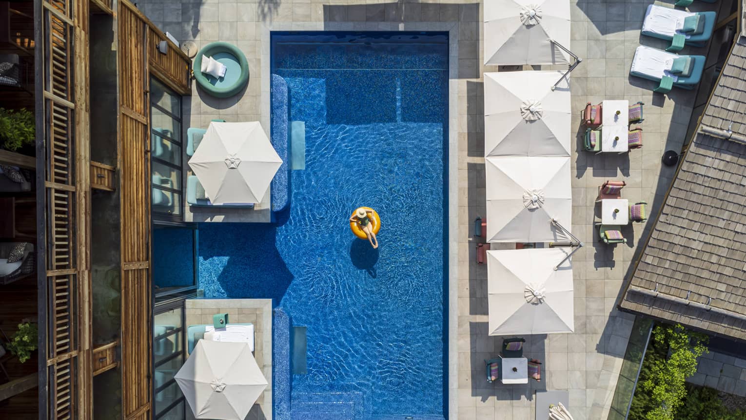 A person in a tube in an outdoor pool surrounded by umbrellas and chairs.