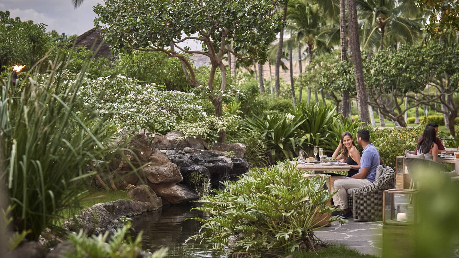 Couple sitting at table surrounded by lush greenery at contemporary outdoor restaurant