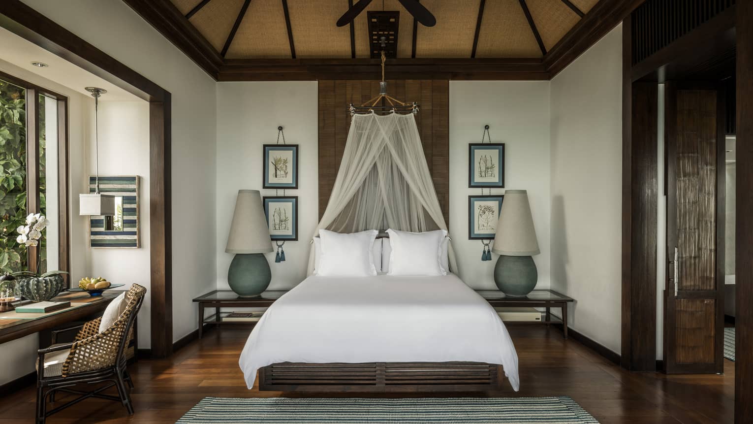 Family Pool Villa bed with white net canopy, large lamps on each side, wood floors, desk by window