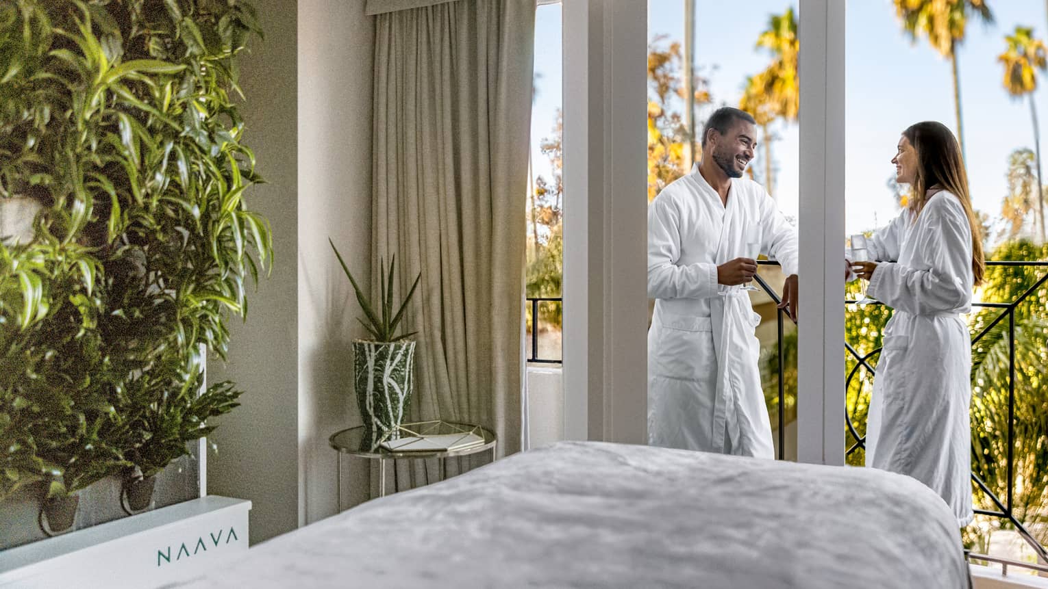 Two guests standing on a balcony wearing spa robes and holding wine glasses.