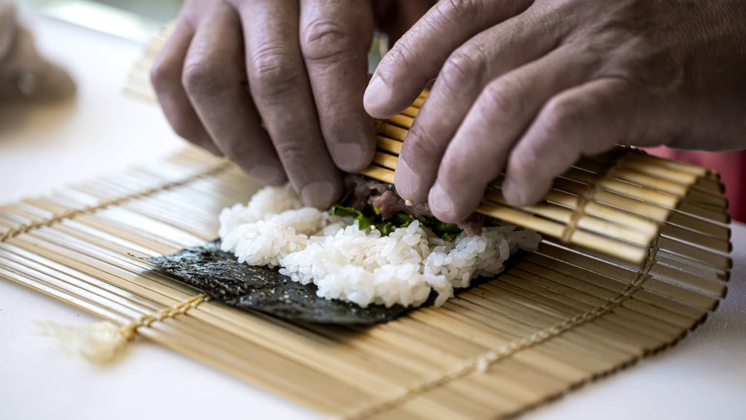 A four seasons chef rolls sushi with a bamboo mat 