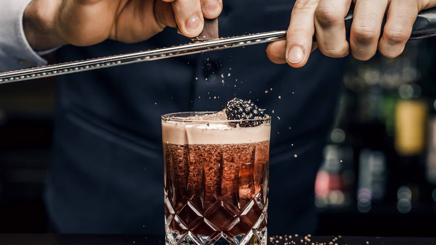 Churchill Club bartender shaves garnish over cocktail in crystal rock glass with blackberry