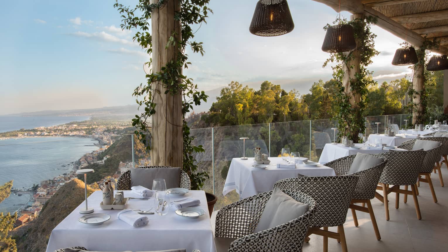Outdoor restaurant terrace lined with 2-person tables, glass railing and sea view