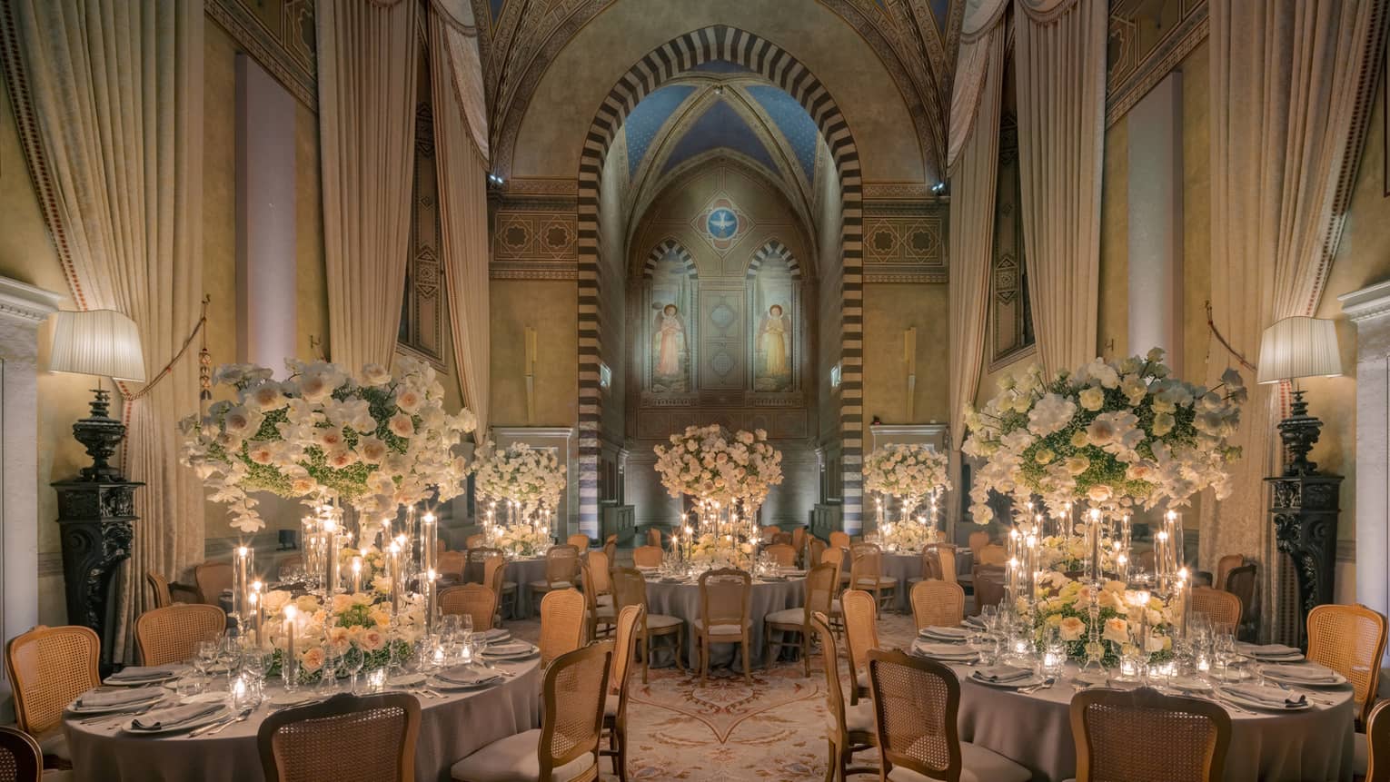 Grand dining room with tall arched ceilings and round elegantly set tables with tall white flower centrepieces