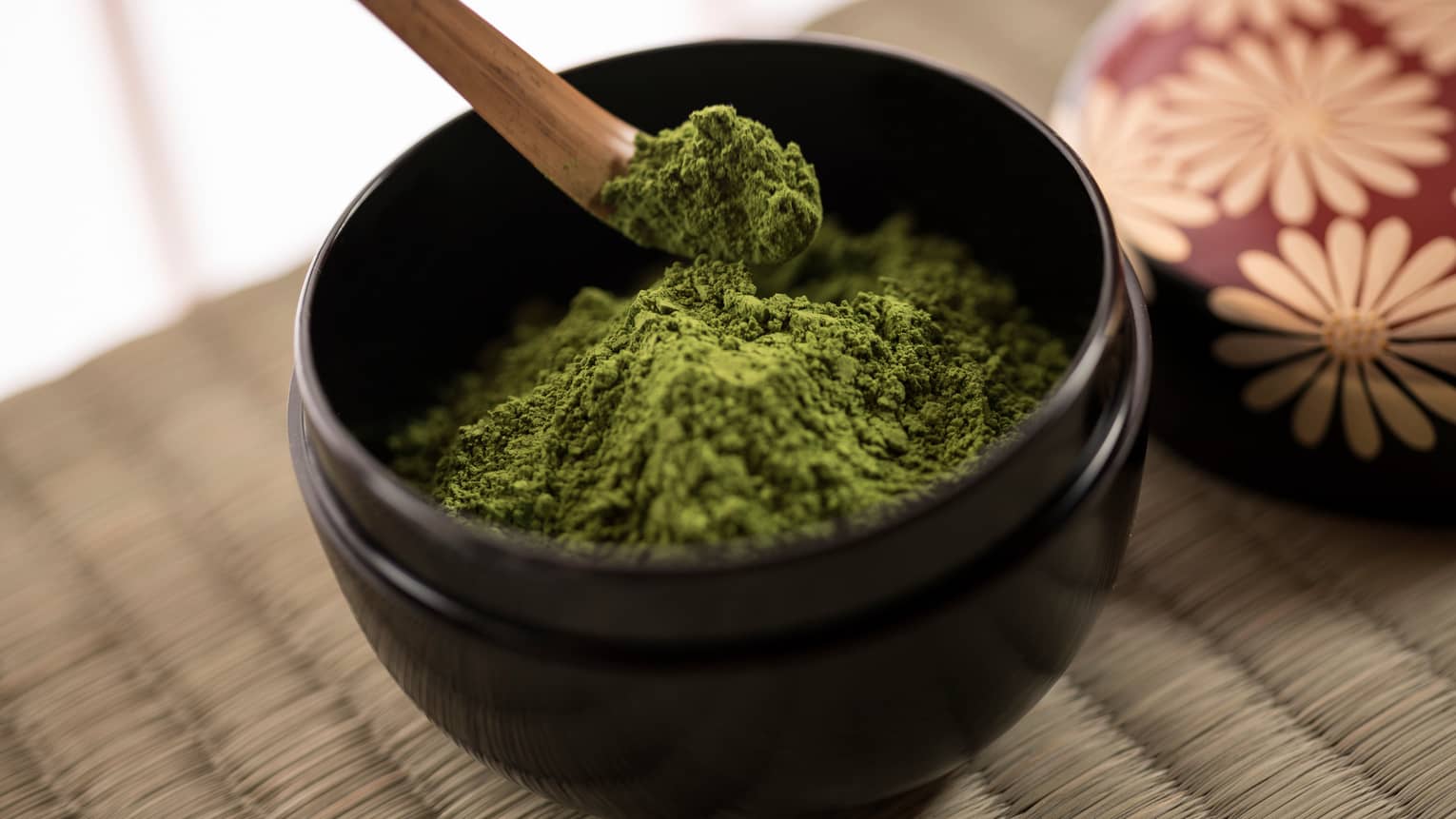 Close-up of green matcha tea powder in small black bowl, wood spoon