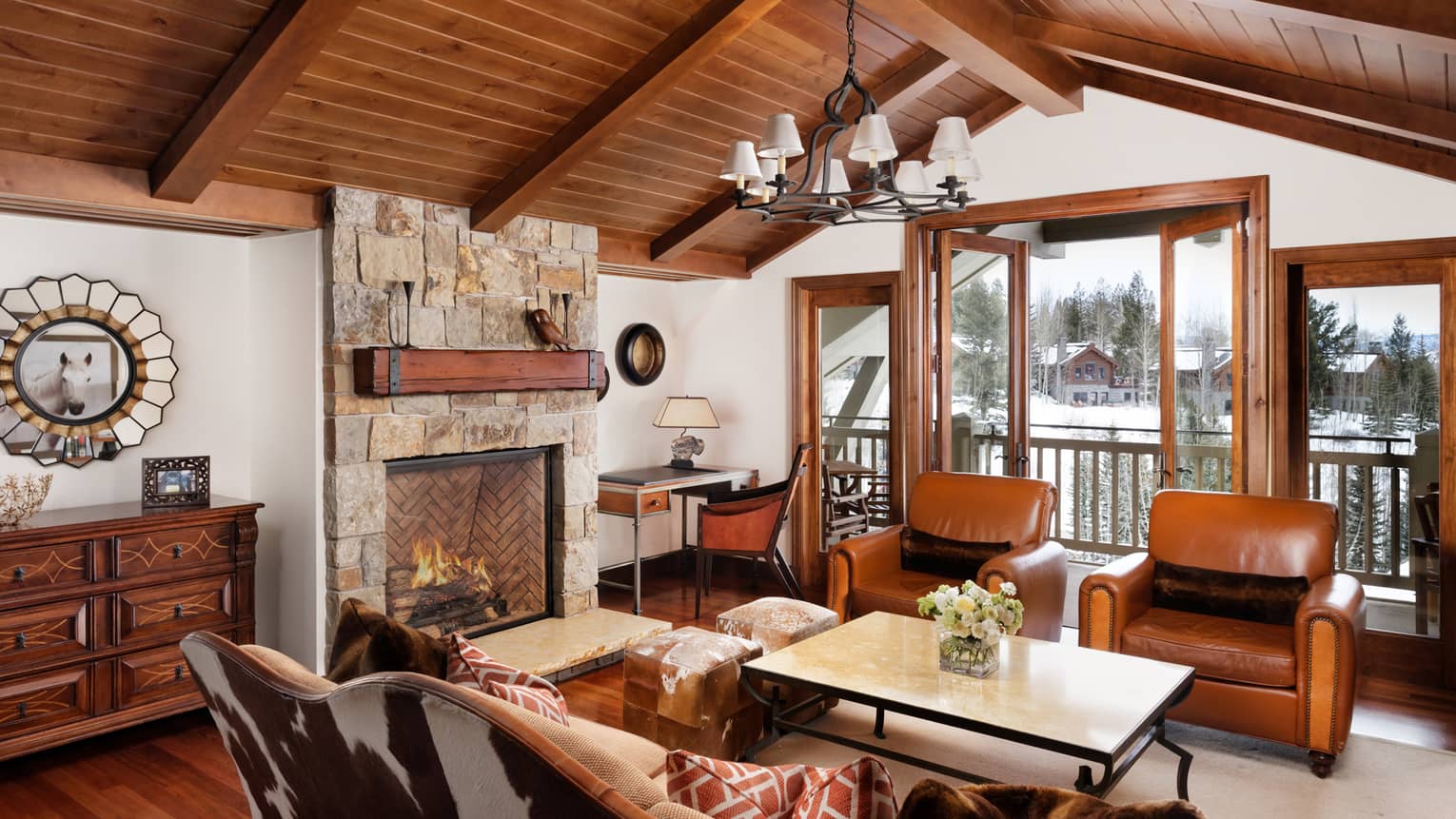 Cowhide sofa, leather armchairs. stone fireplace under arched wood beam ceiling
