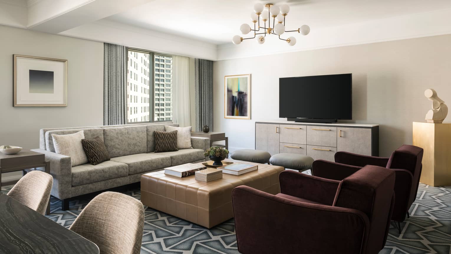 Living room with beige sofa, large square coffee table, two burgundy arm chairs, graphic carpeting