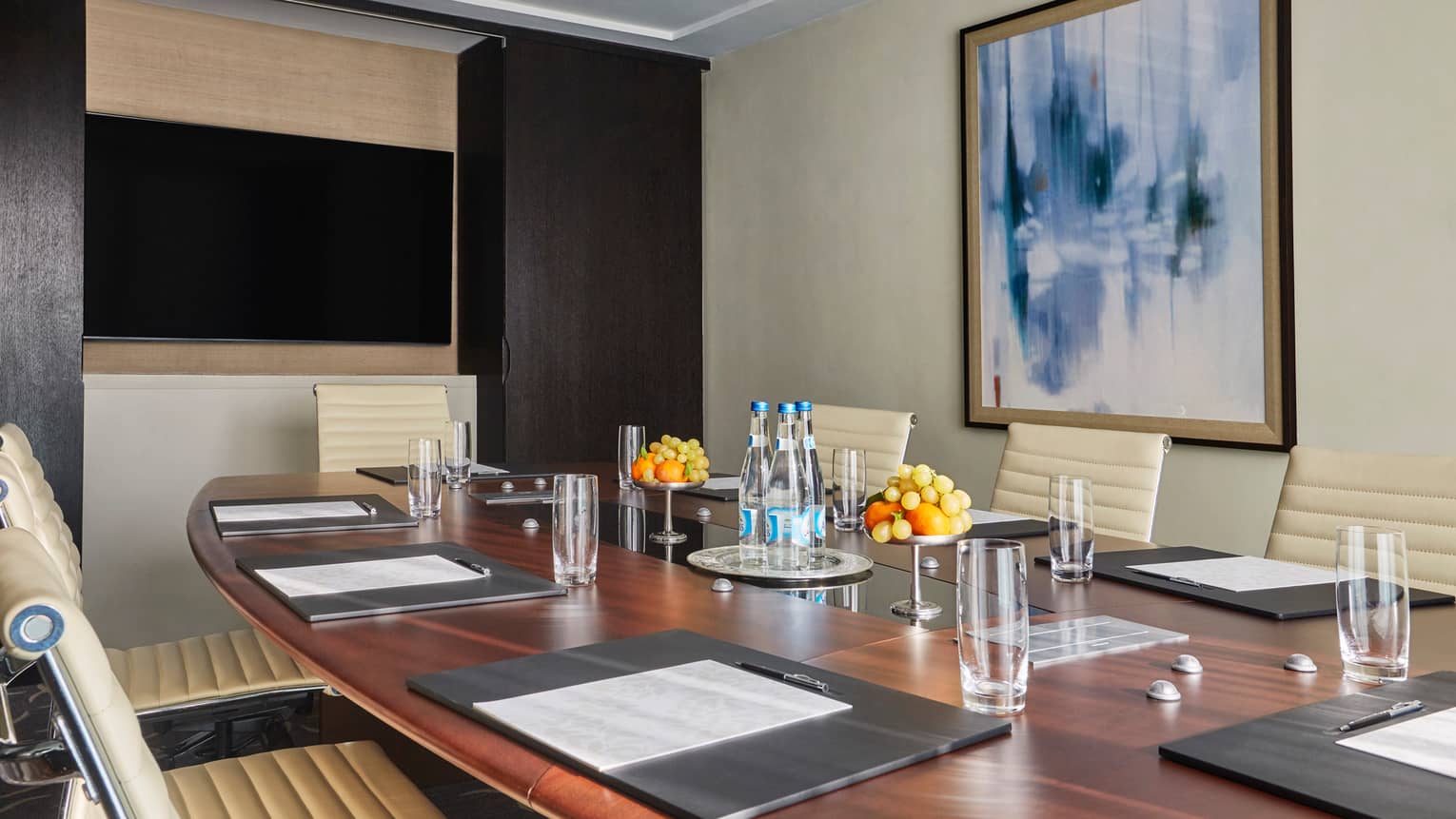 Large wood meeting room table with glasses, bottles of water, fresh fruit