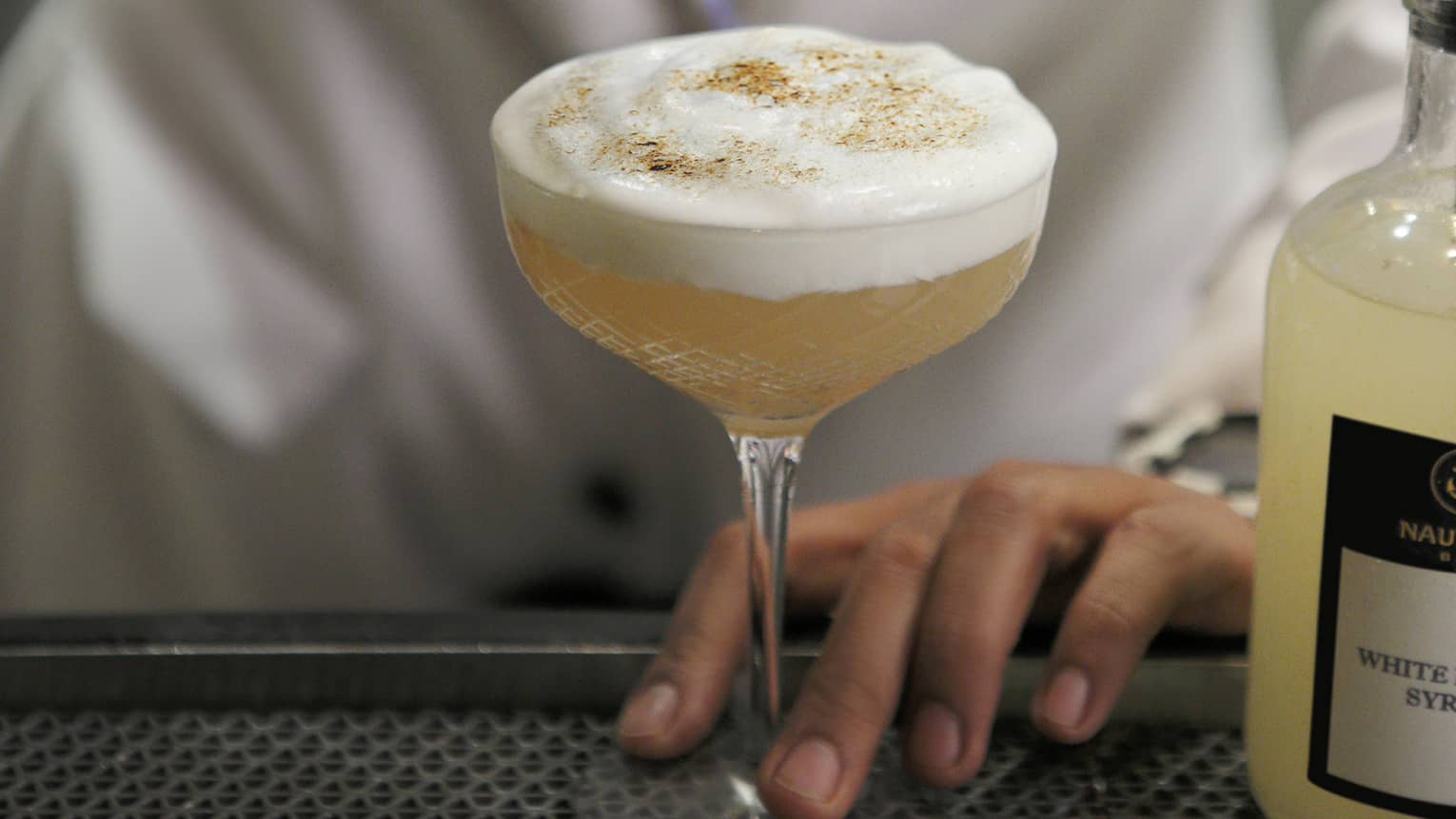 Close-up of mixologist lighting torch over foamy cocktail on bar