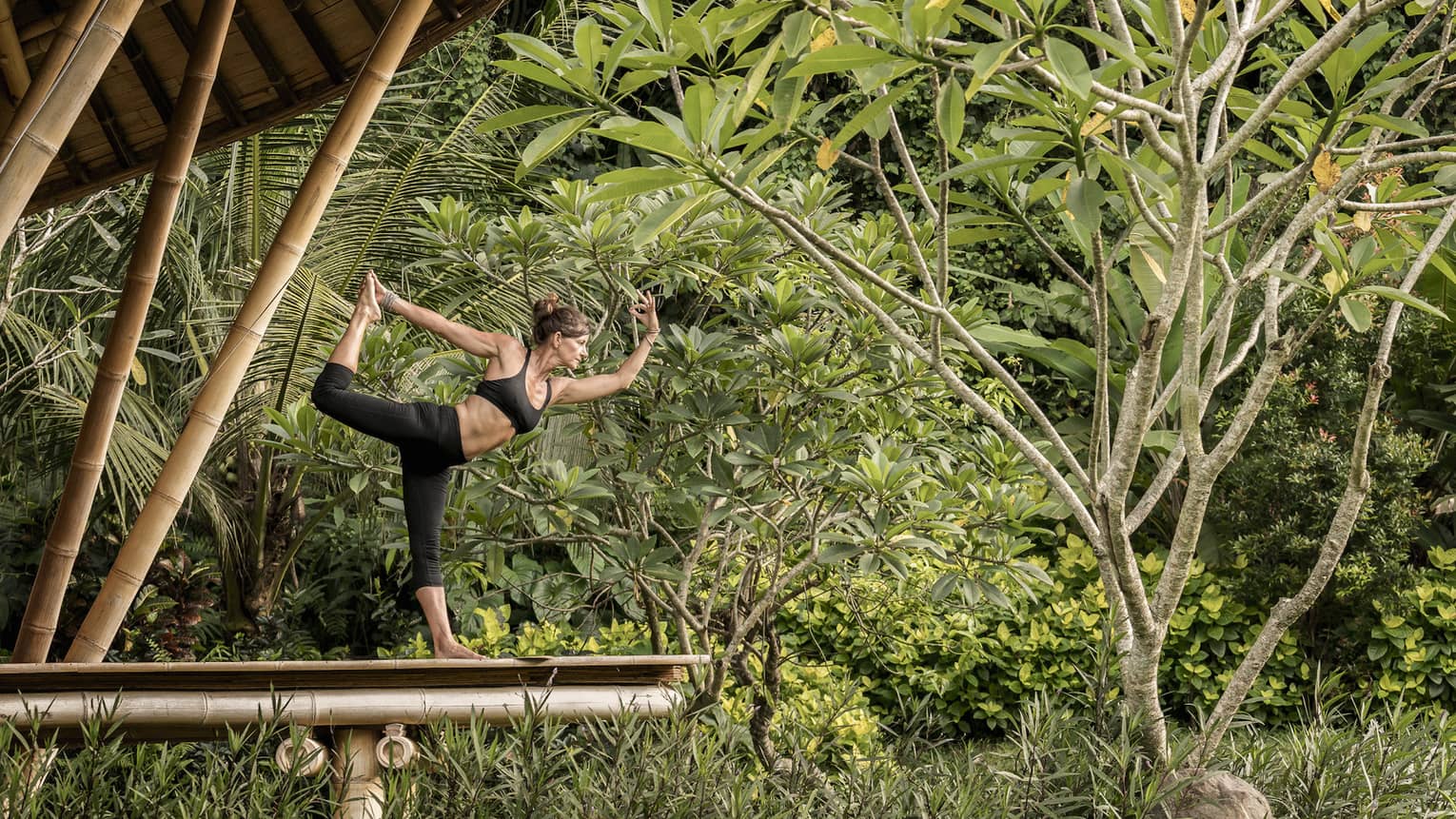 A guest with her arms and leg outstretched, doing yoga in an outdoor pavilion 