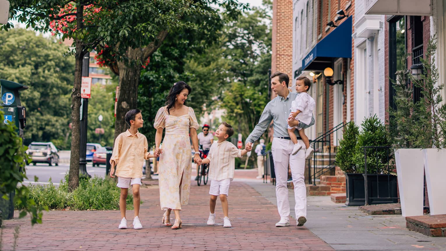 Man, woman and three children walk on cobblestone street near shops