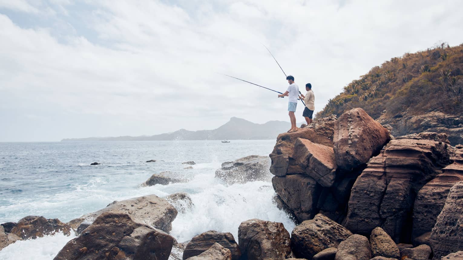 Two men on large rocks fishing in the ocean.