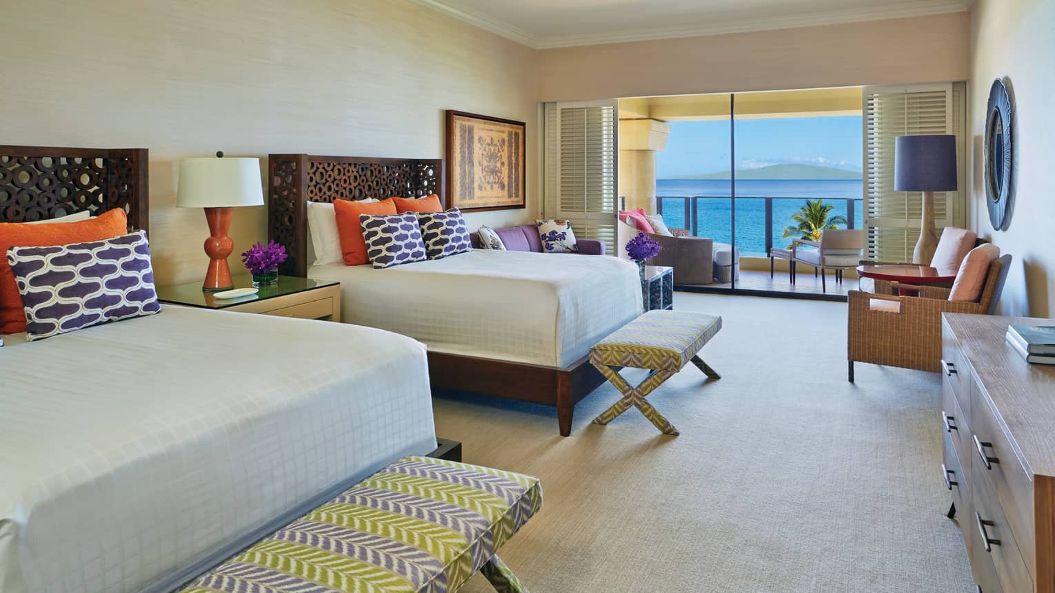 Spacious presidential suite with two queen beds, colourful pillows and a balcony overlooking the ocean at a tropical resort