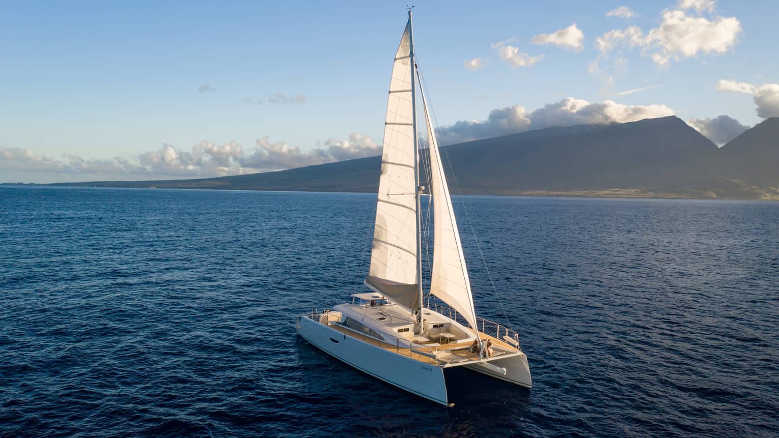 Catamaran sailing on the open water against a mountain backdrop