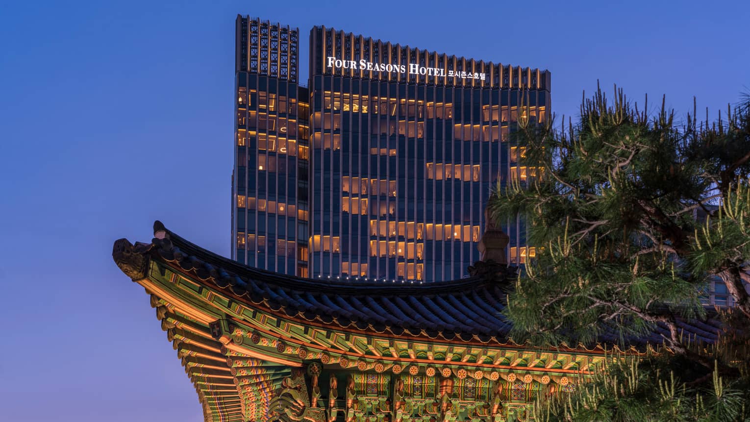 Four Seasons Hotel Seoul modern glass high rise with lights towering over traditional building at night