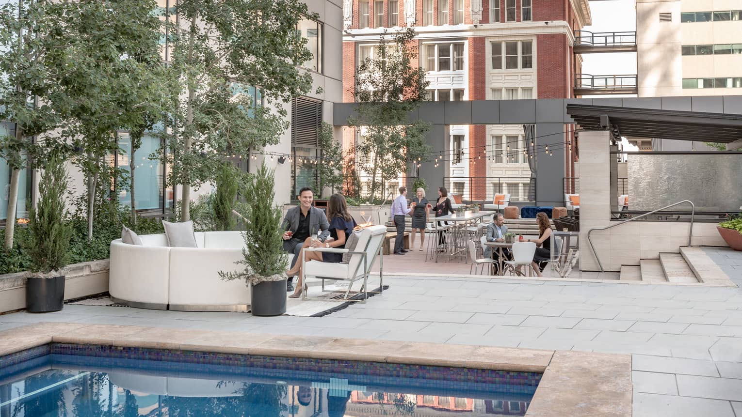 Couples, friends wearing business attire enjoy cocktails on outdoor patio lounge by swimming pool