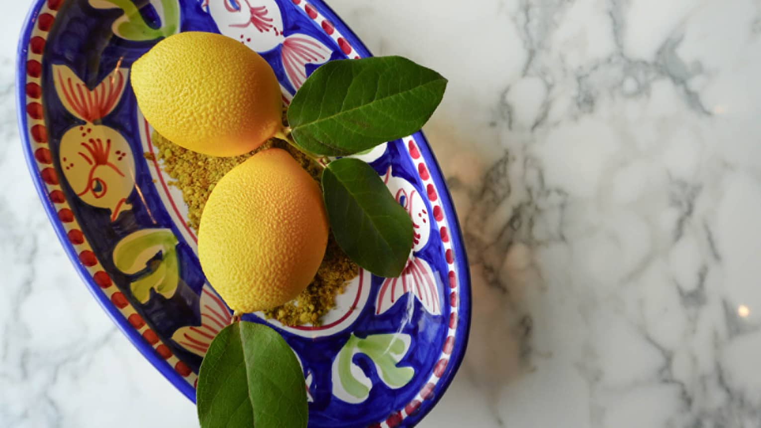 Lemons in a blue bowl with yellow and white fish painted on it.
