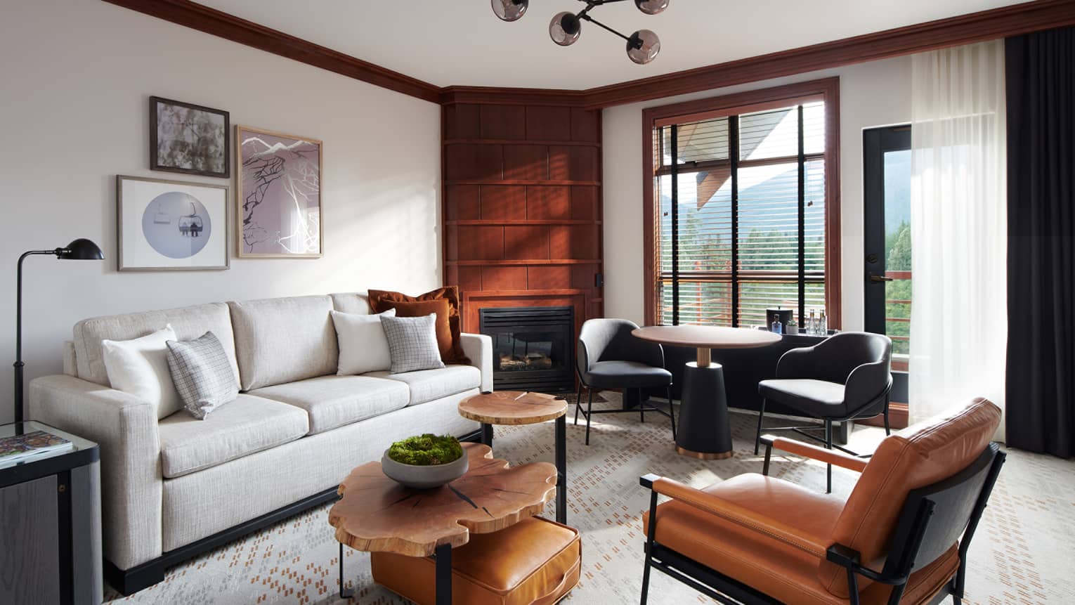 Living room with cream couch, wooden nesting tables, brown leather accent chair, window with view of foliage