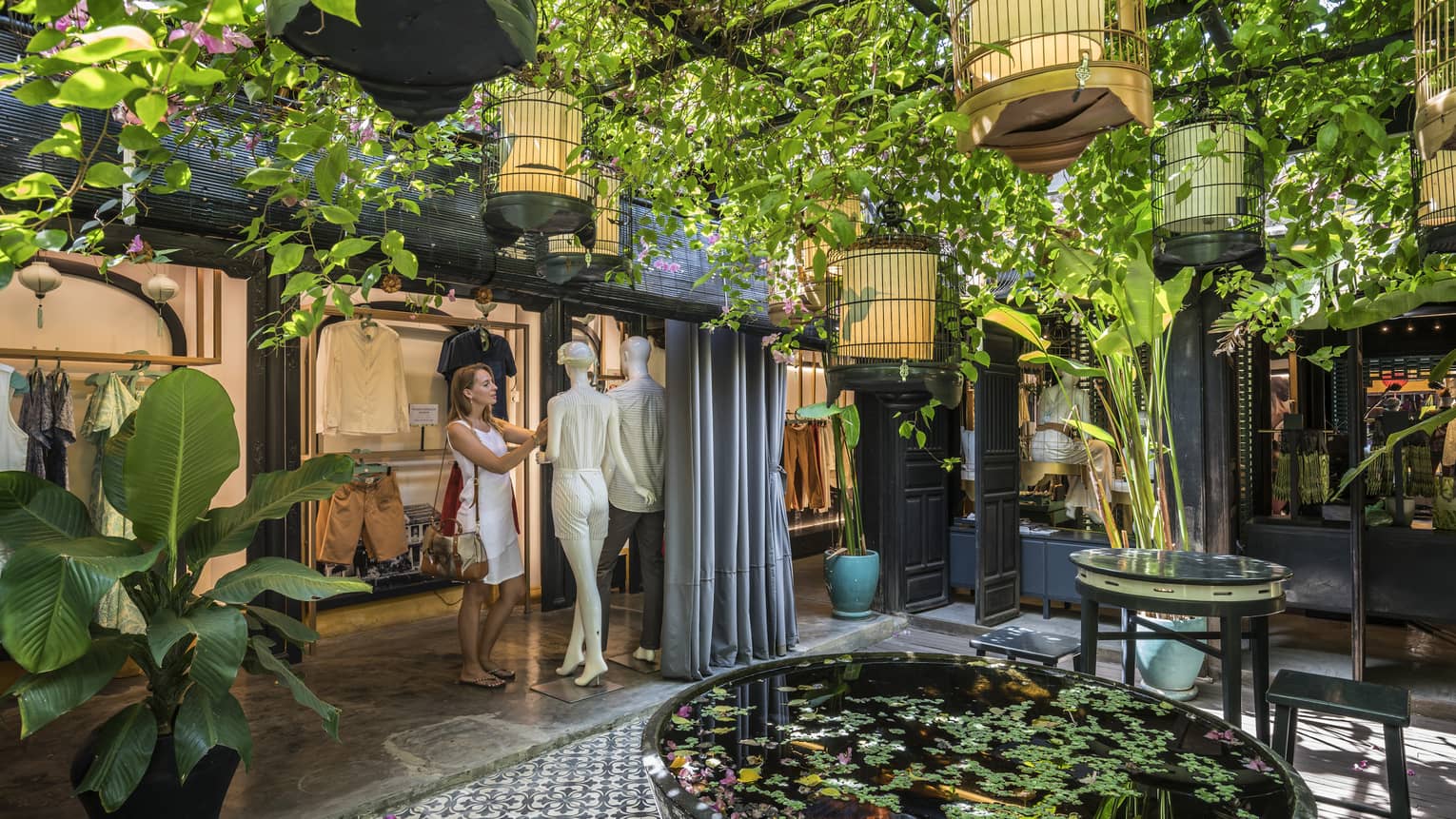 A woman looking at a mannequin in a shopping area with lots of plants and natural lightin Hoi 