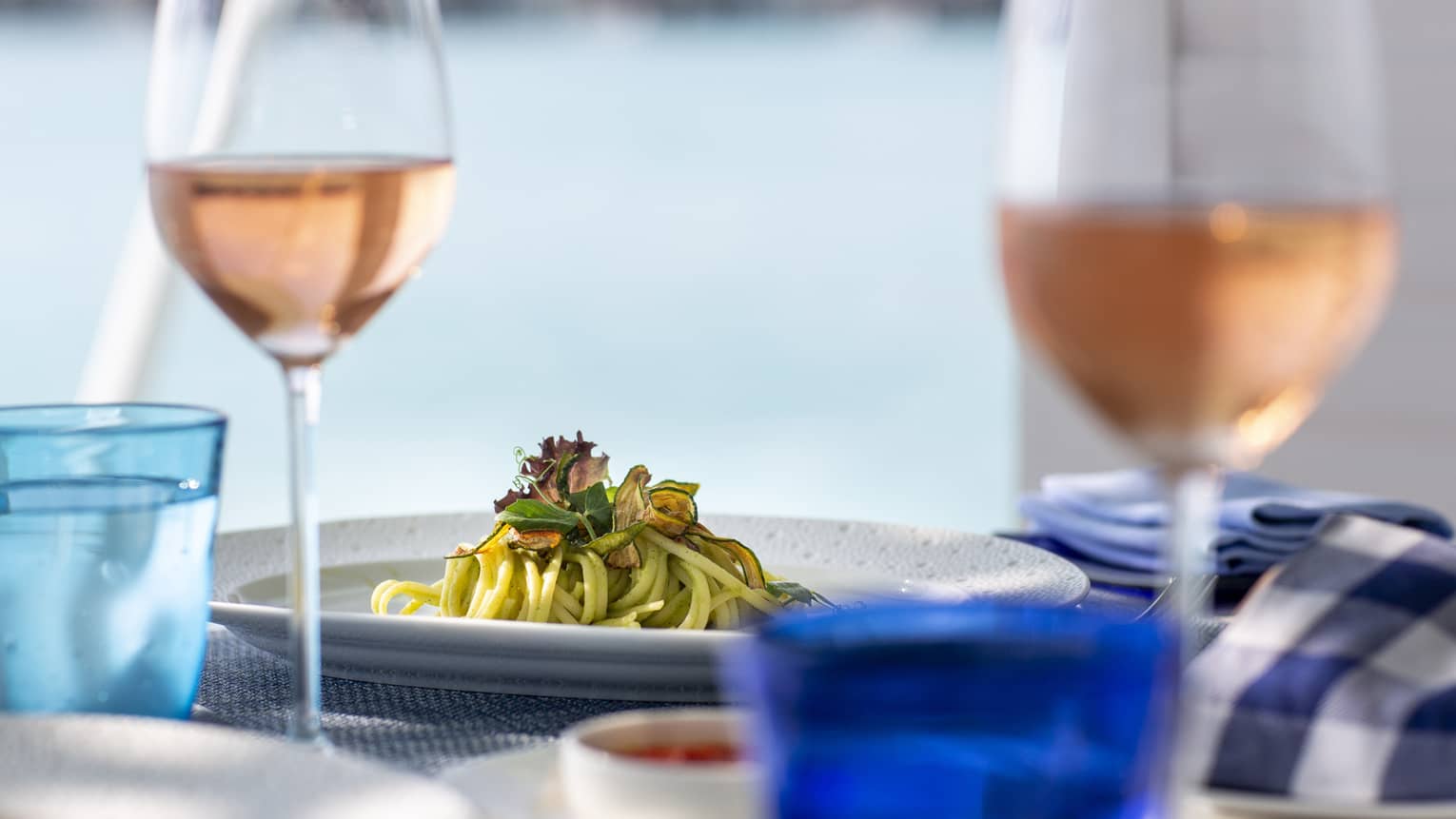 A side view of a table with glasses of rose and a pasta dish over looking the ocean in Four Seasons Maldives - Landaa
