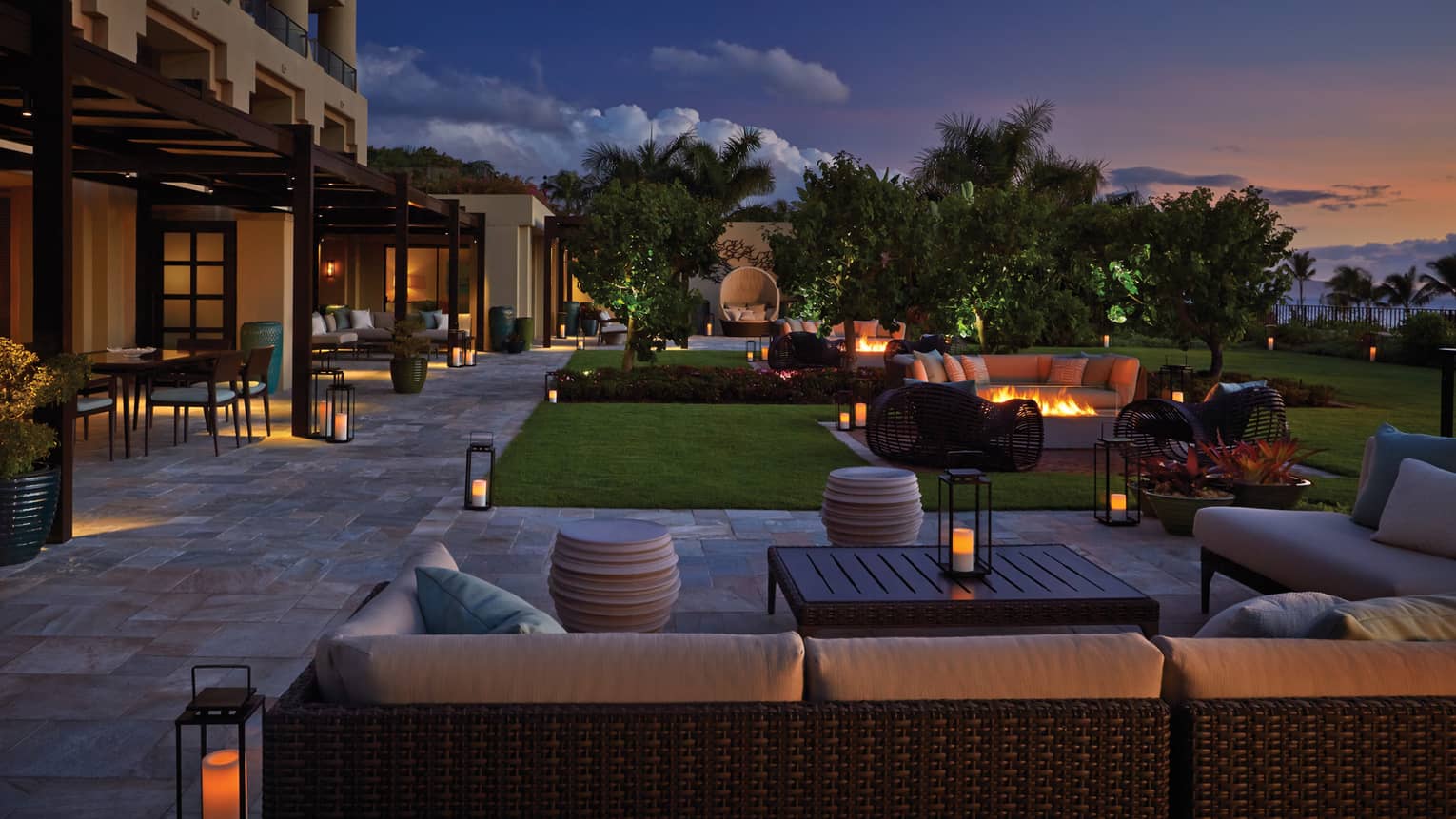 Outdoor suite garden with seating, fire pits and lanterns at dusk, surrounded by lush greenery and palm trees at a luxury resort