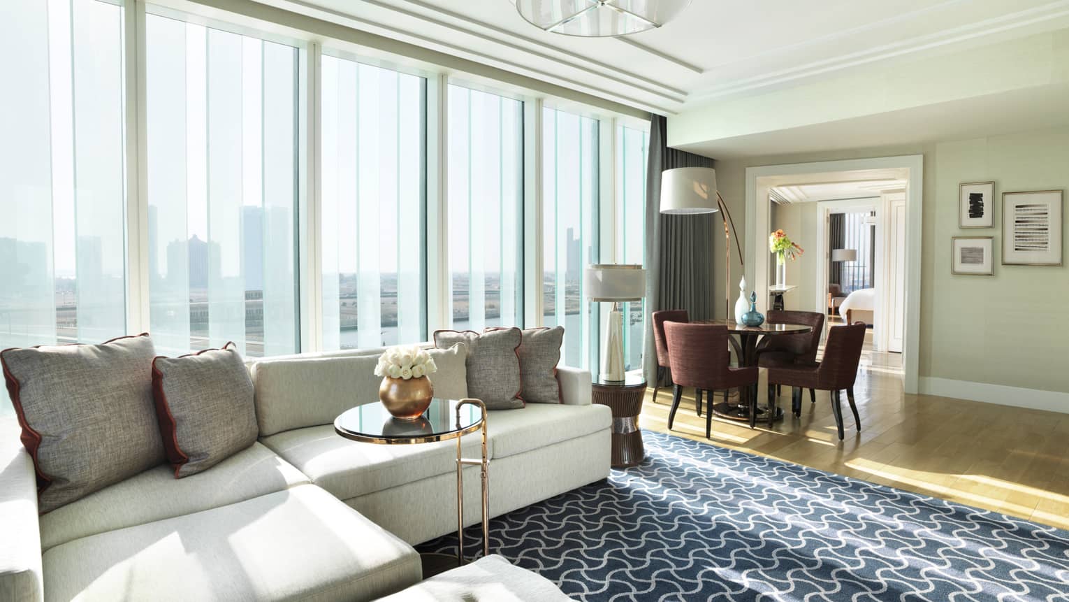 Deluxe Four Seasons Executive Suite large living room with L-shaped white sofa against large window, dining table