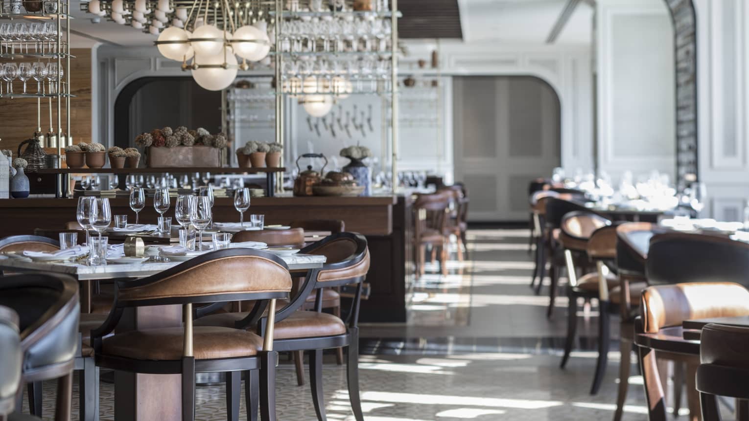 Sunny La Capitale dining room with elegant brown leather chairs, tables, white tile, modern globe chandeliers