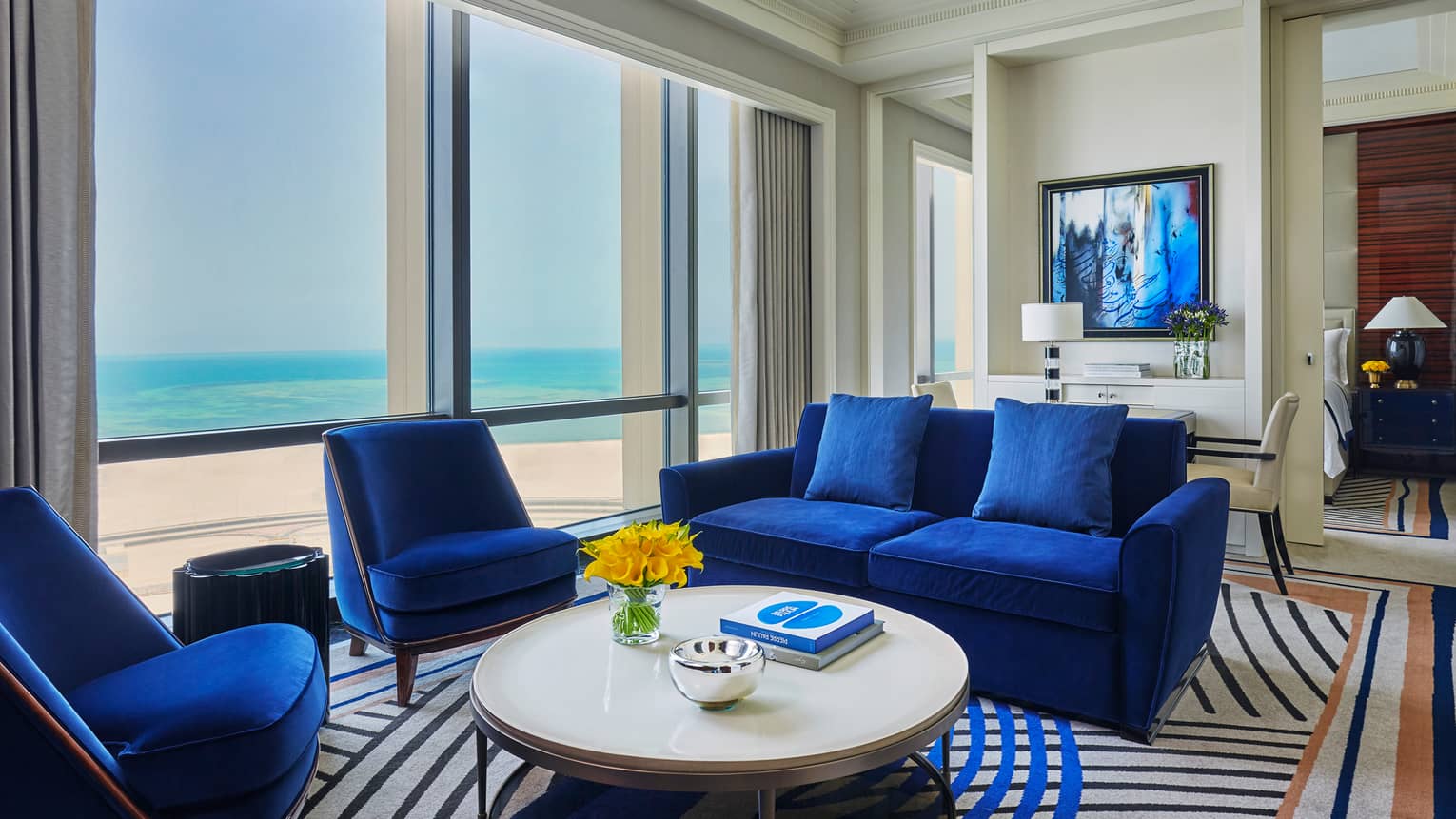 Four Seasons Executive Suite living area with blue velvet loveseat, chairs, round coffee table, sunny windows