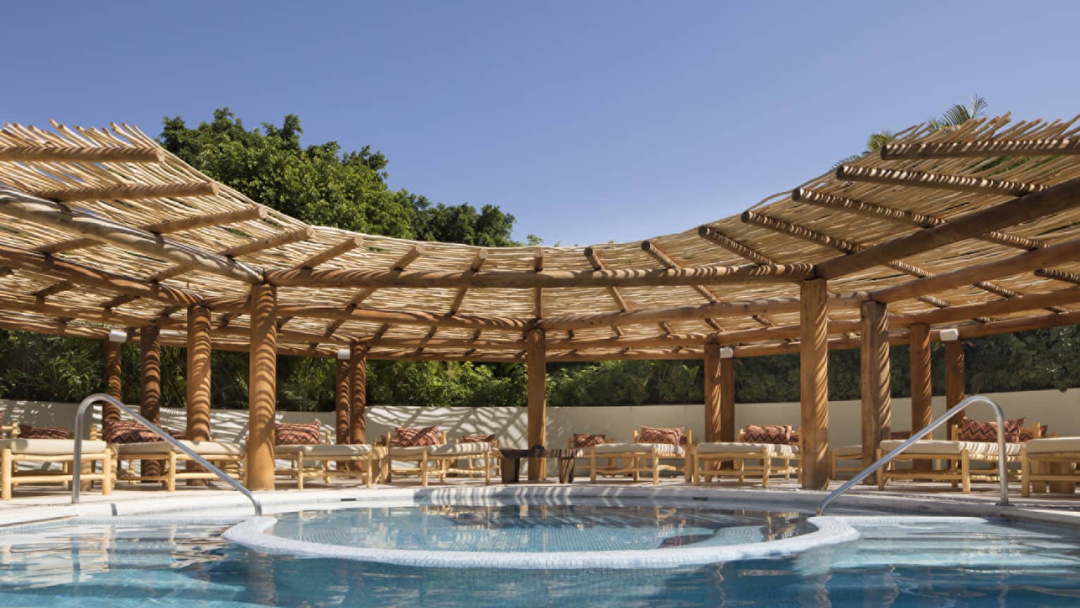Resort pool with two entries and lounge chairs under thatched-roof awning