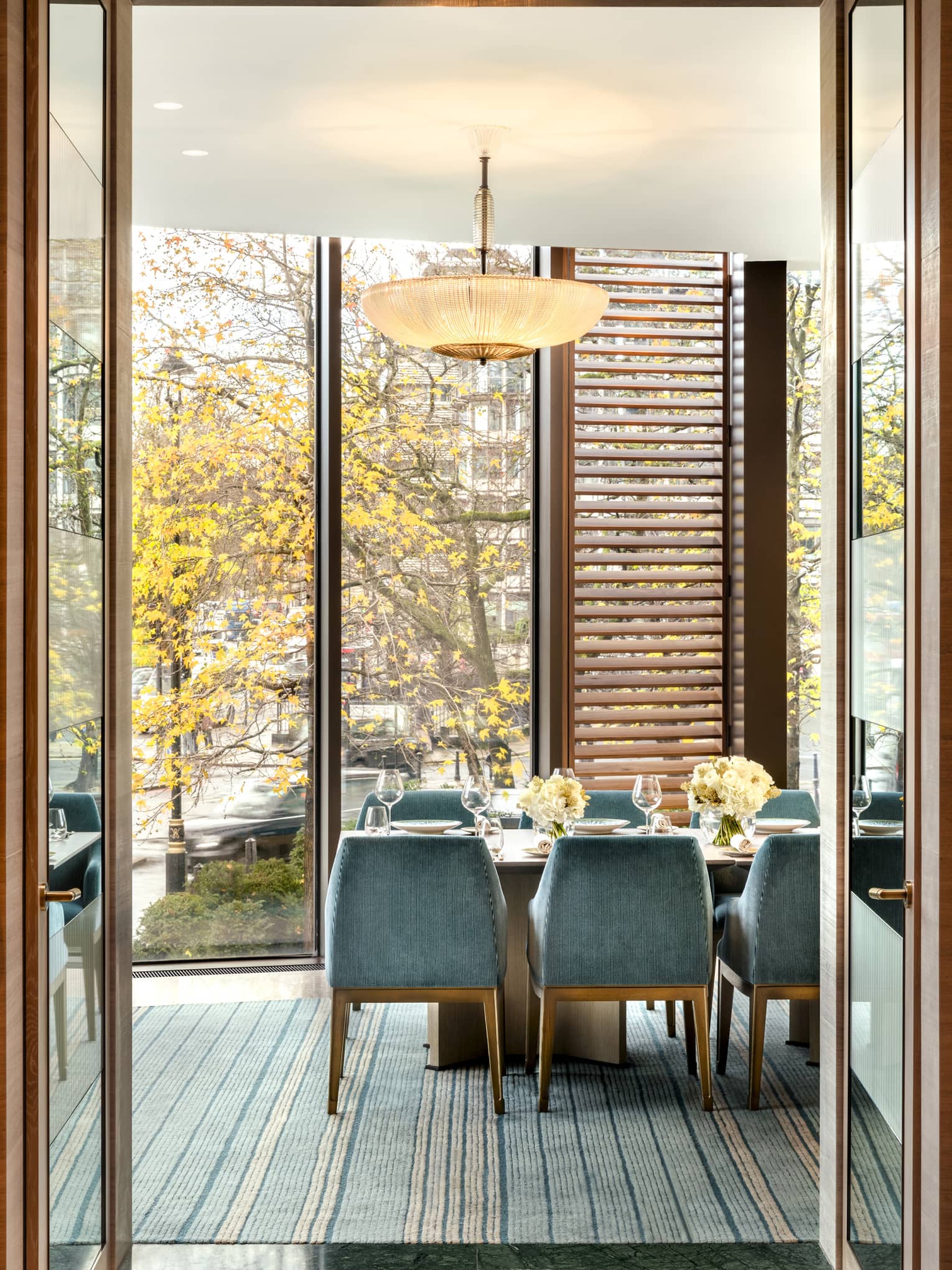 Bright dining area with table flanked by blue suede chairs and beside tall windows