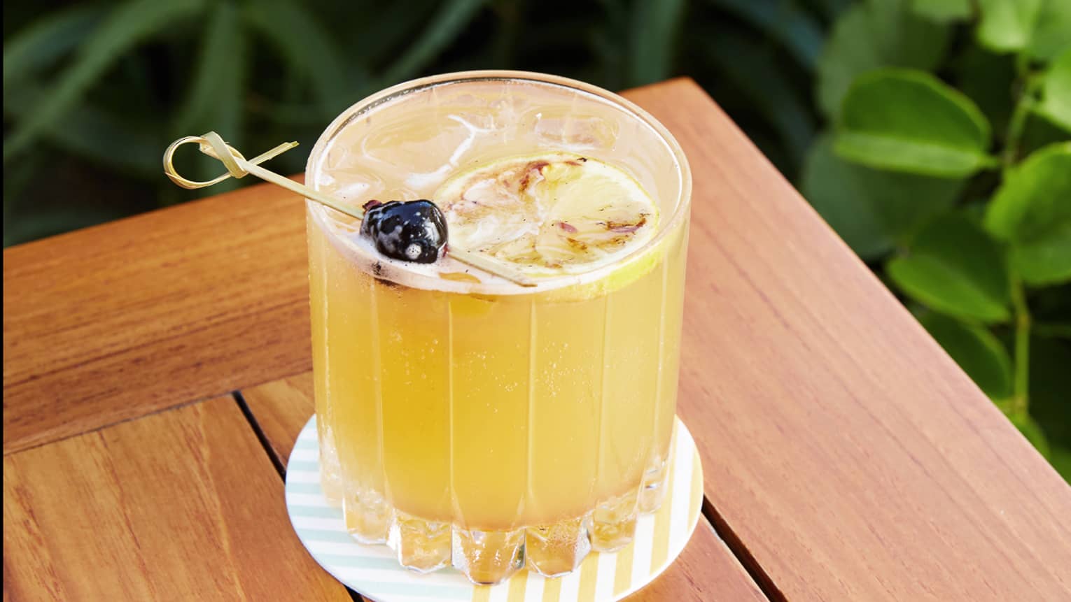 Yellow drink in a glass on a coaster on an outdoor table.