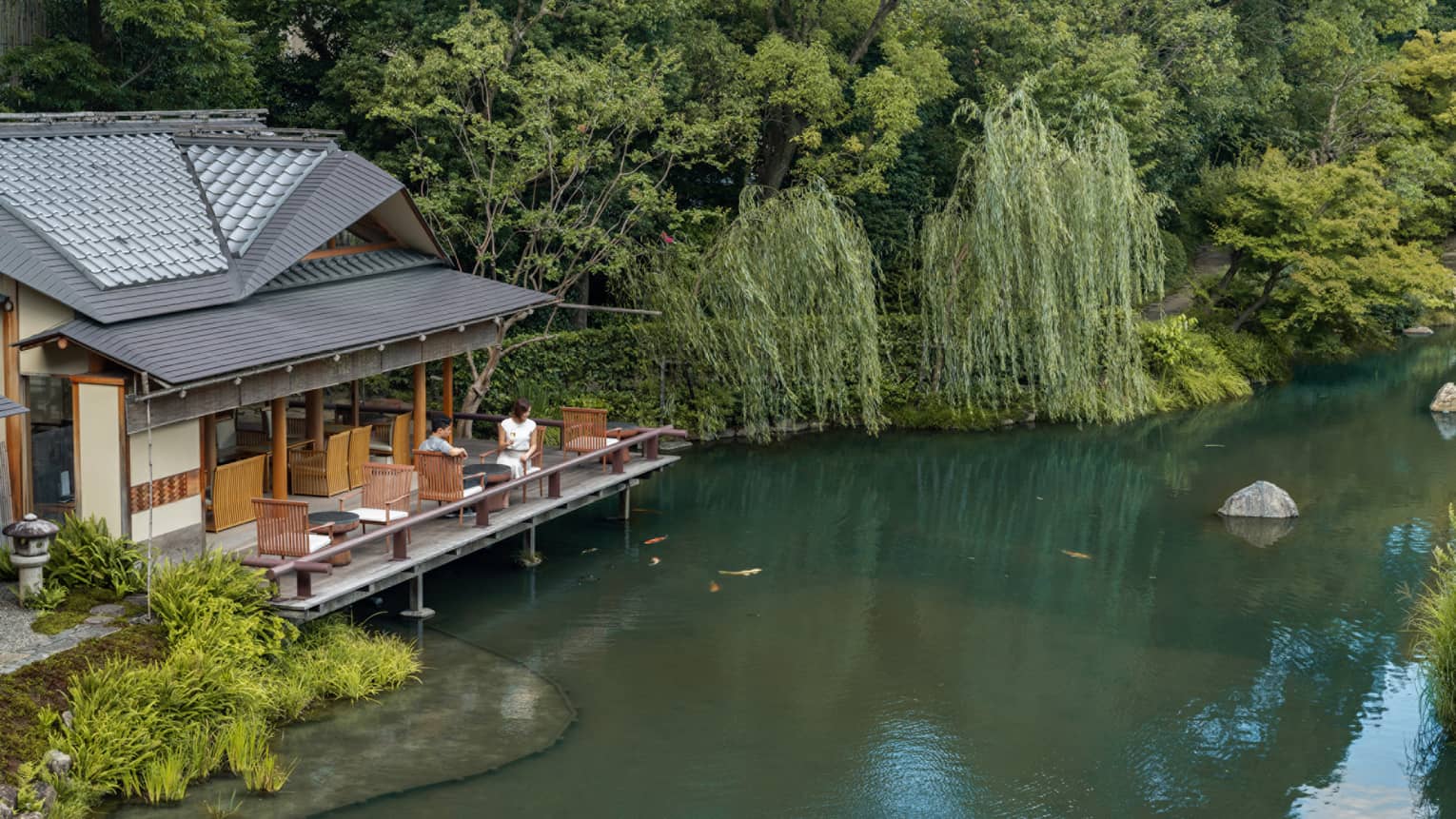 Two guests sit on the outdoor terrace of a pagoda overlooking the koi pond