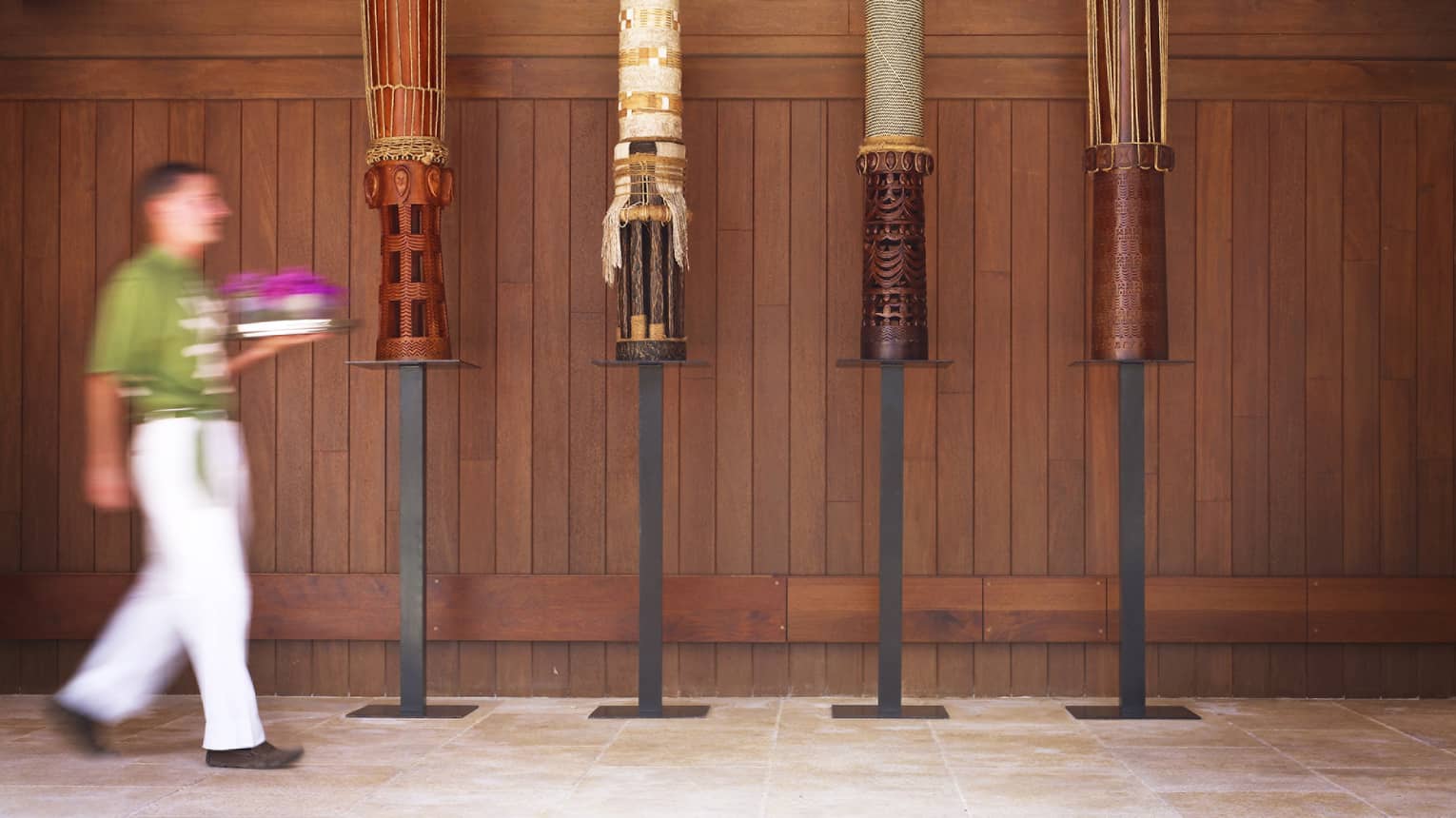 hotel staff carries tray past art installation with four tall drums under cathedral ceiling