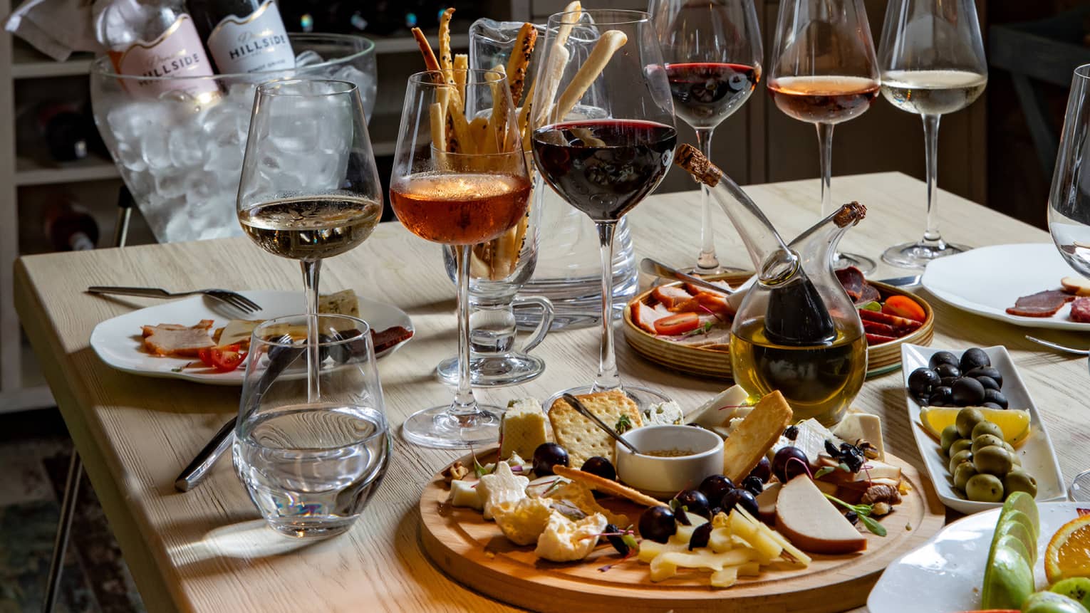 In a dimly lit room with exposed brick walls, a table is set with half-full wine glasses and appetizing hors-d’oeuvres. 