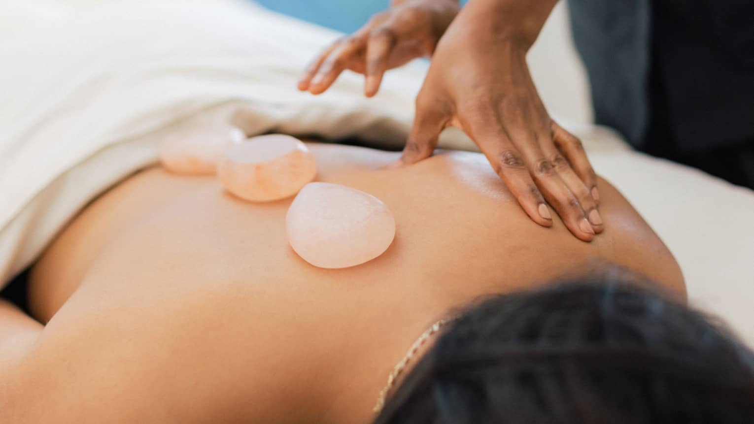 Masseuse places salt stones on a person's bare back