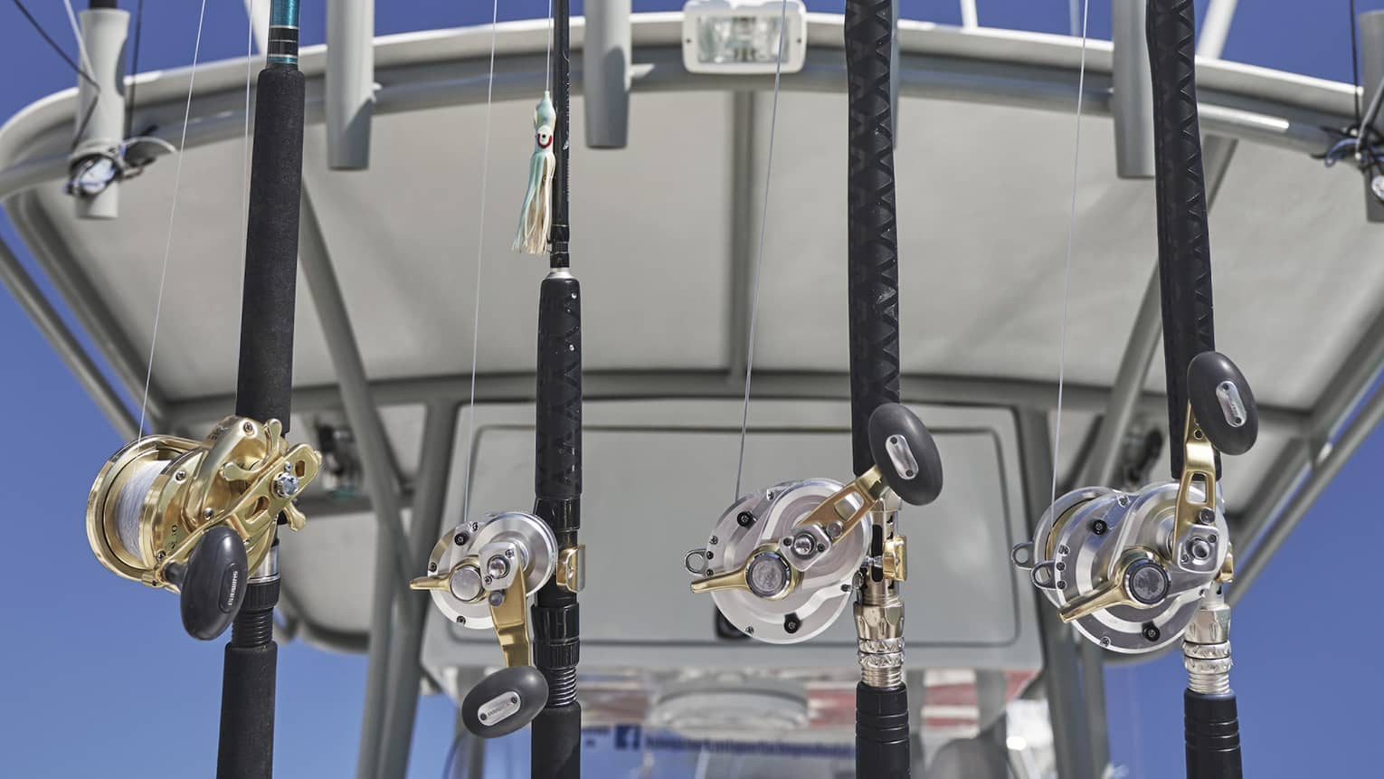 Close-up shot of ten upright fishing rods in a rack attached to a boat’s Bimini top, a clear, dark blue sky behind them.