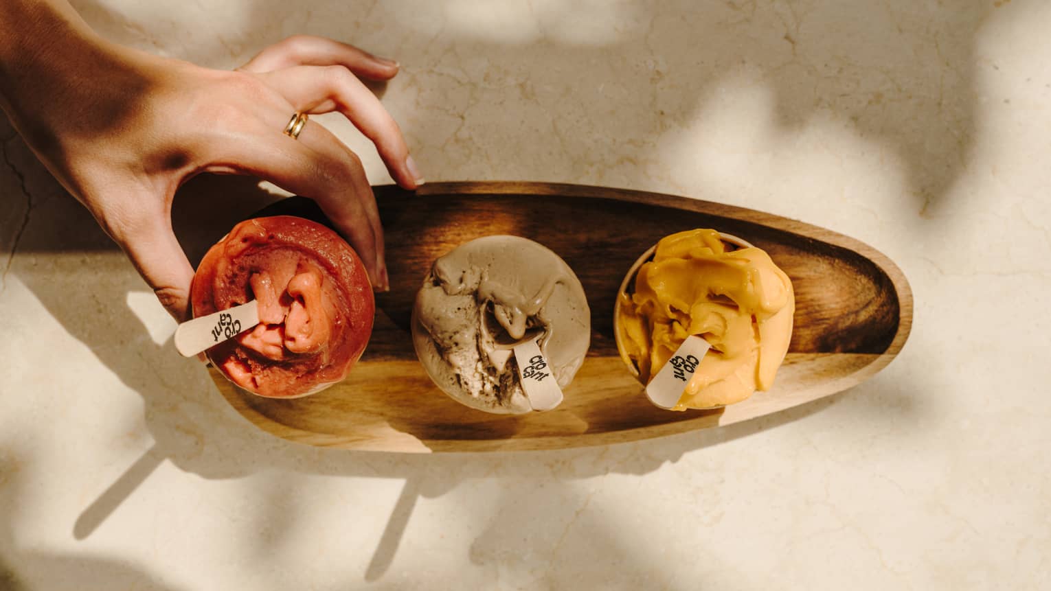 A person places cups of ice cream on a wood serving tray.