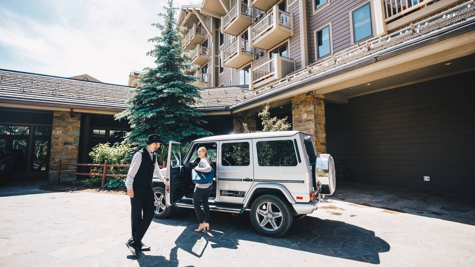 Resort staff opens the driver-side door of a luxury utility vehicle parked in the driveway for guest