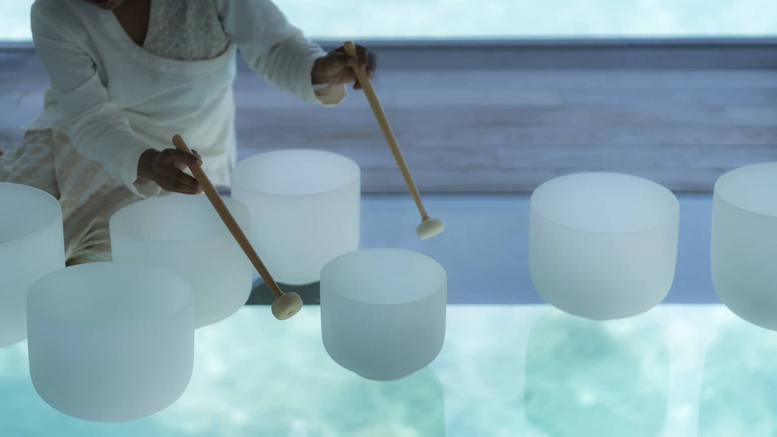 Spa staff plays various white crystal bowls with wood mallets during sound healing session